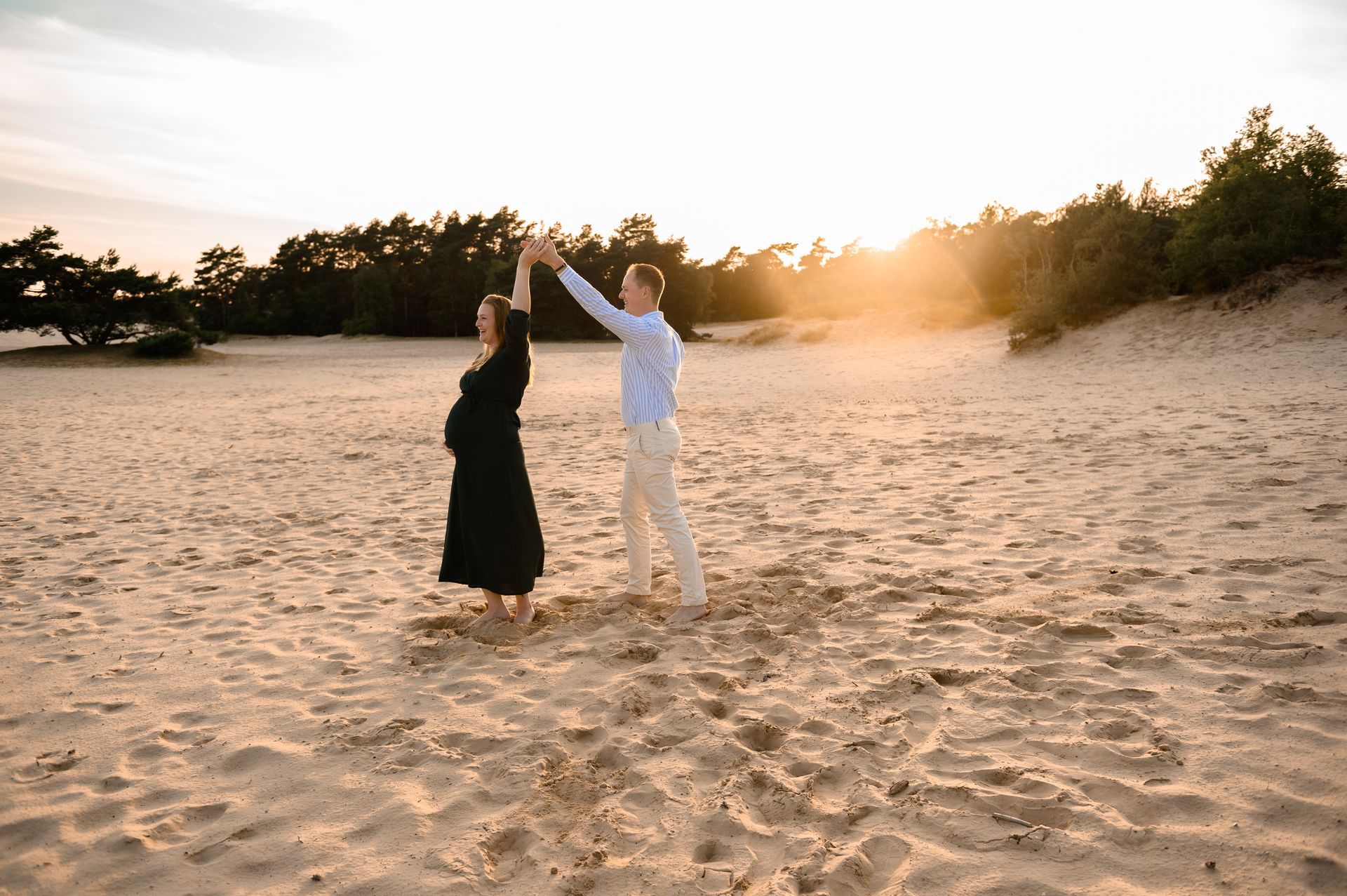 Een stel danst op het zand met de armen omhoog, de zon gaat onder op de achtergrond.