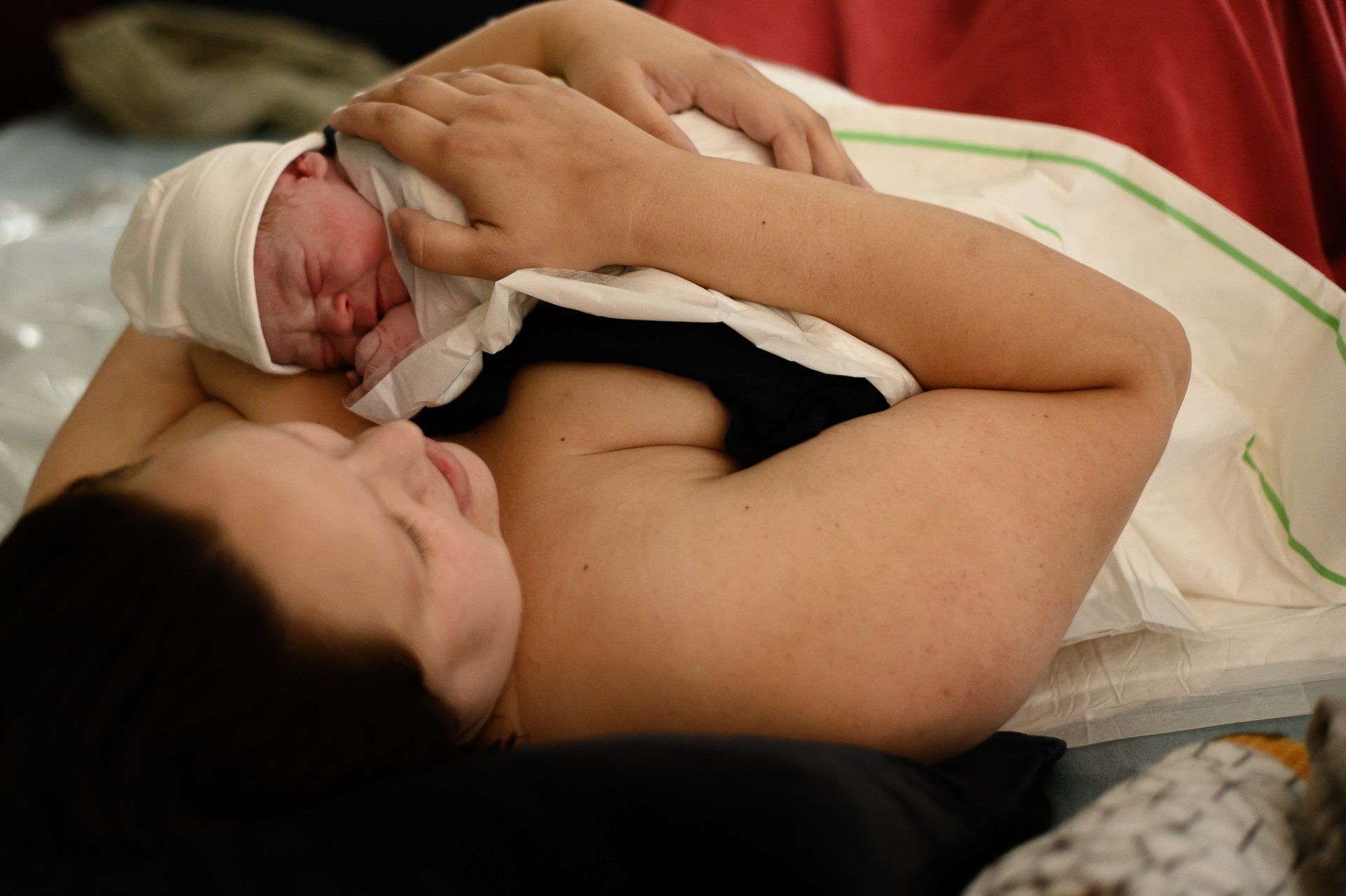 Pasgeboren baby rustend op de blote borst van de moeder; ziekenhuisomgeving.