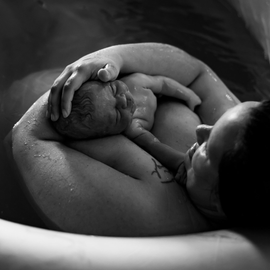 Moeder wiegt pasgeboren baby in een bevalbad en houdt de baby dicht tegen zich aan. Zwart-wit.