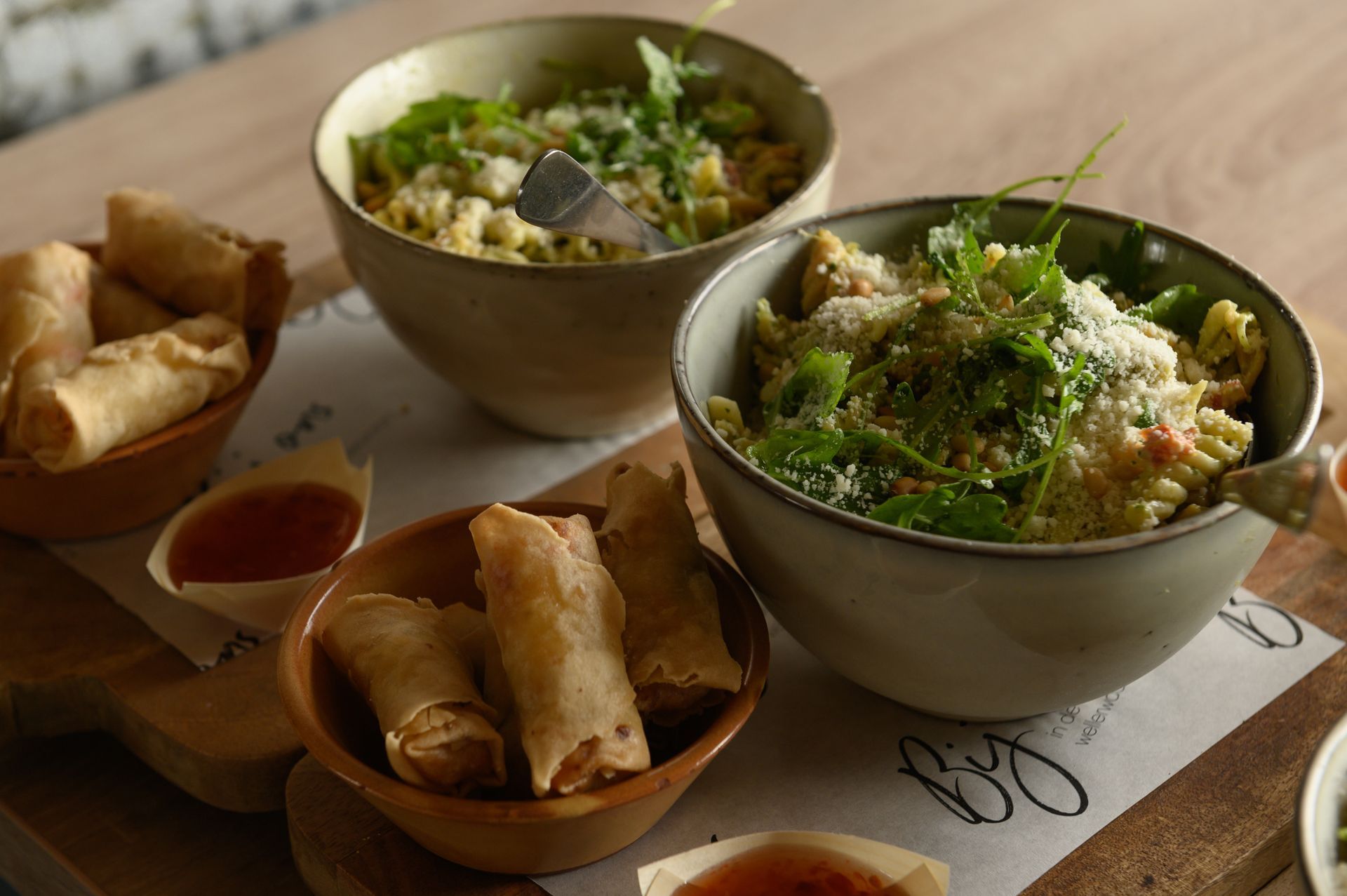 Kommen pasta en rijst met loempia's en dipsauzen op een houten schaal.