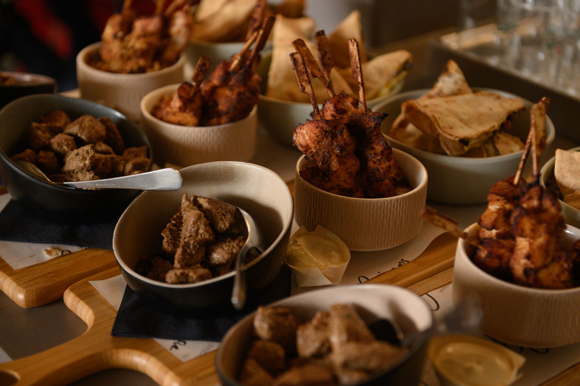 Diverse hapjes in kleine schaaltjes op houten plankjes: gefrituurd vlees, chips en dipsauzen.