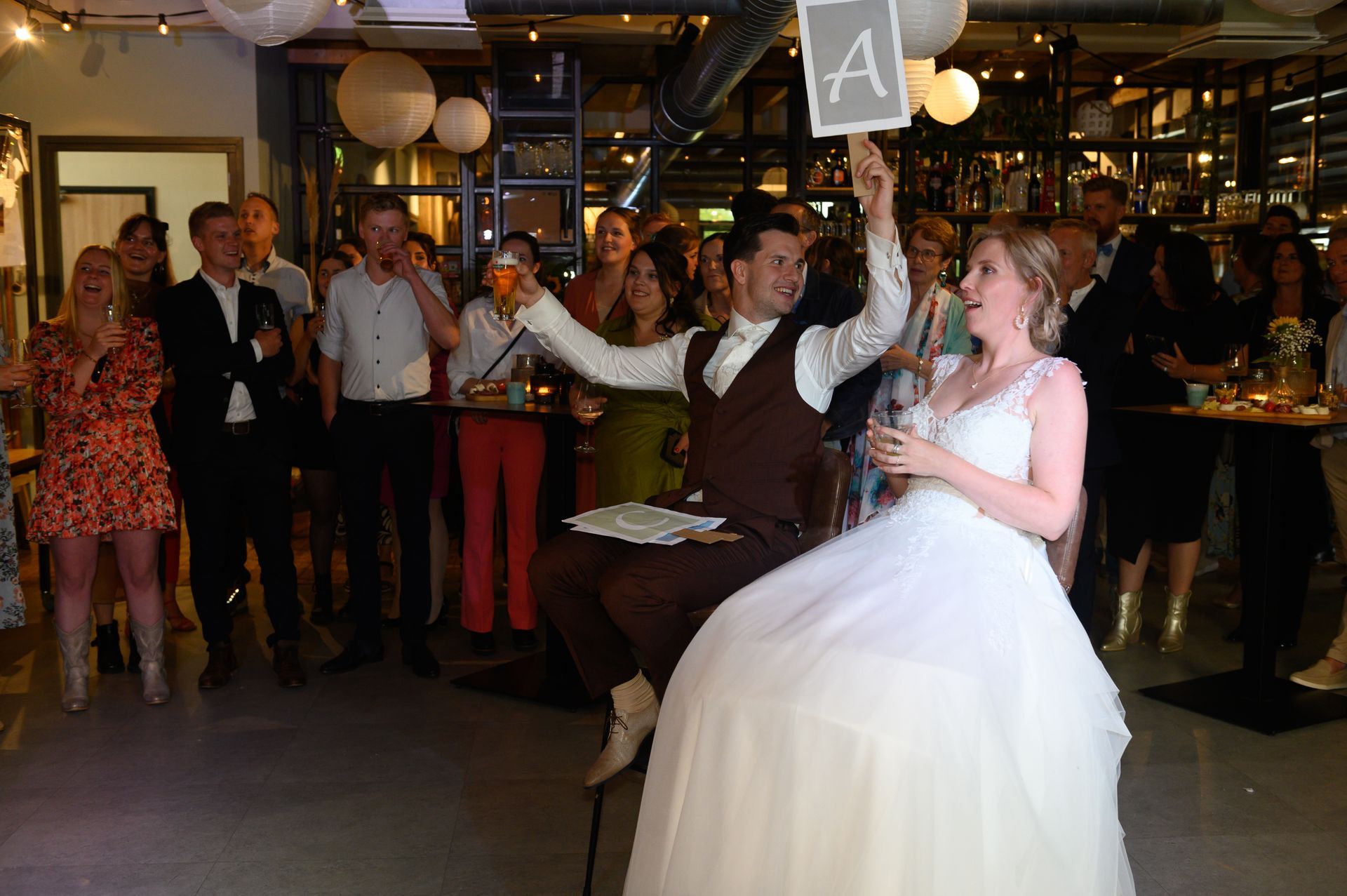Het pasgetrouwde stel op de receptie, de man houdt een bord met de letter 