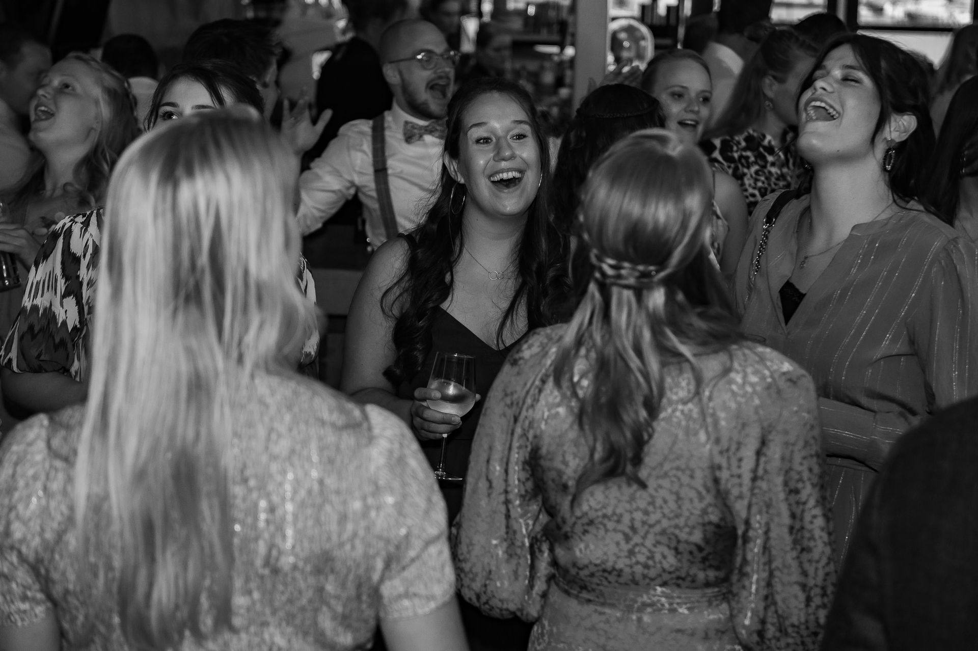 Mensen lachen en dansen op een feest; binnen, sommigen in formele kleding.