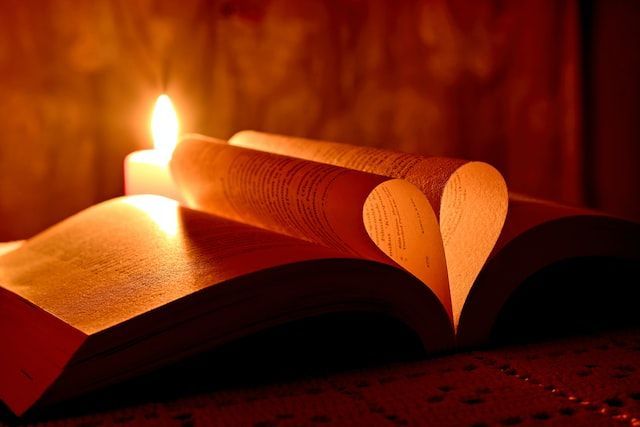 Open book with pages shaped into a heart beside candlelight, symbolizing remembrance, comfort