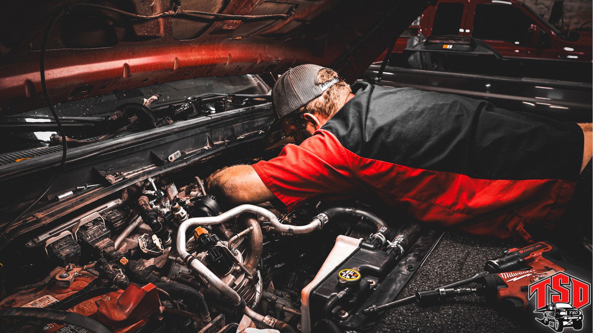 Mechanic in red shirt working on a car engine in a dim garage