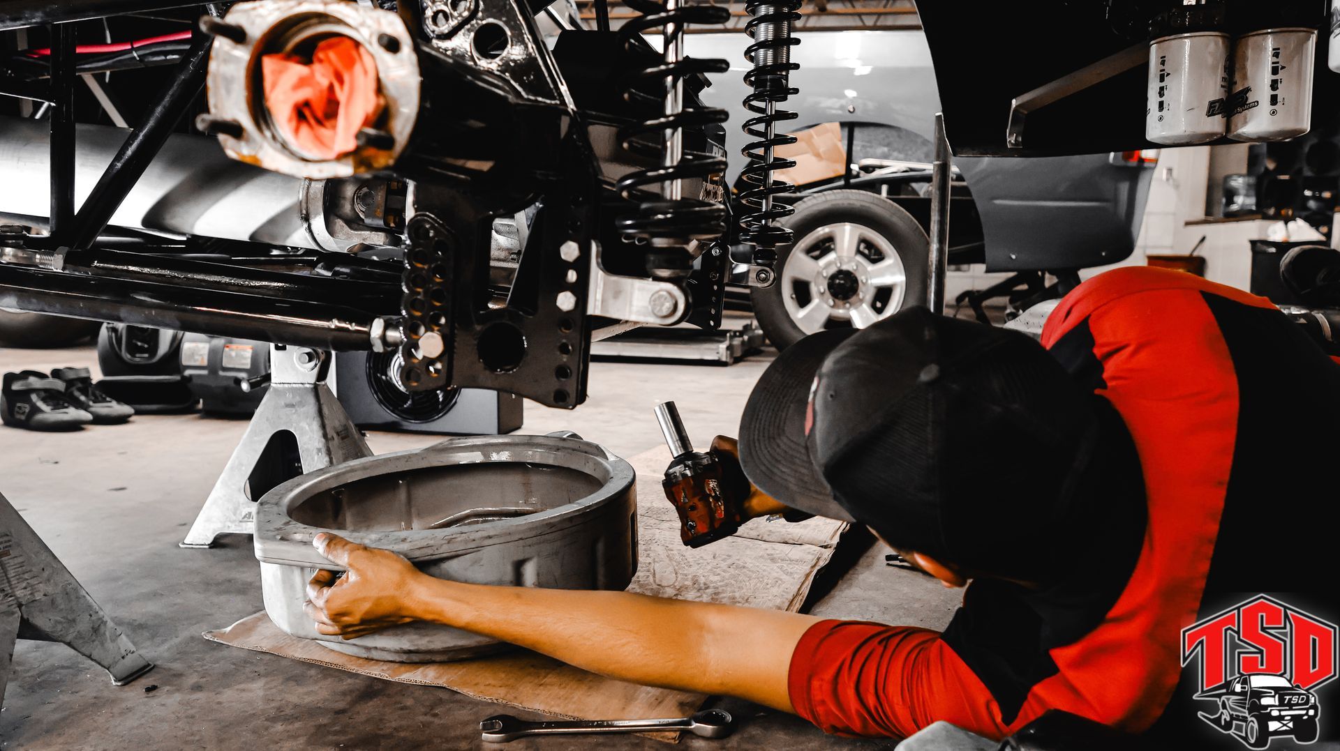 Mechanic under a lifted car, working on a brake assembly in a garage