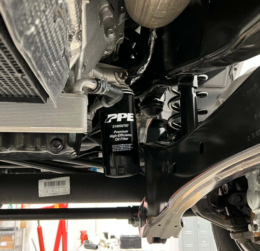 Underbody of a vehicle on a lift, showing a black PPE oil filter and suspension components.