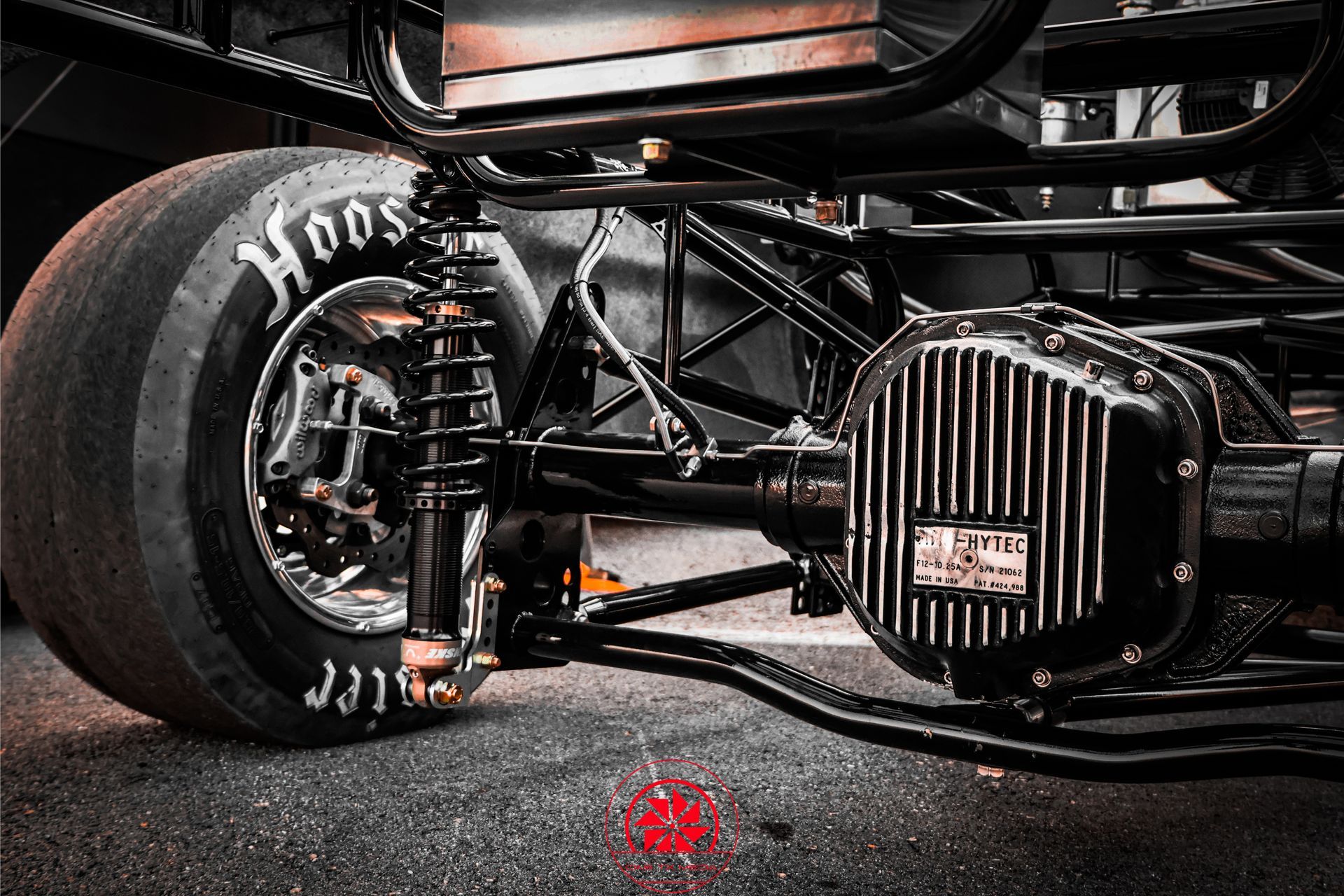 Close-up of a race car’s front wheel and suspension on a track, with a red light reflection on the asphalt