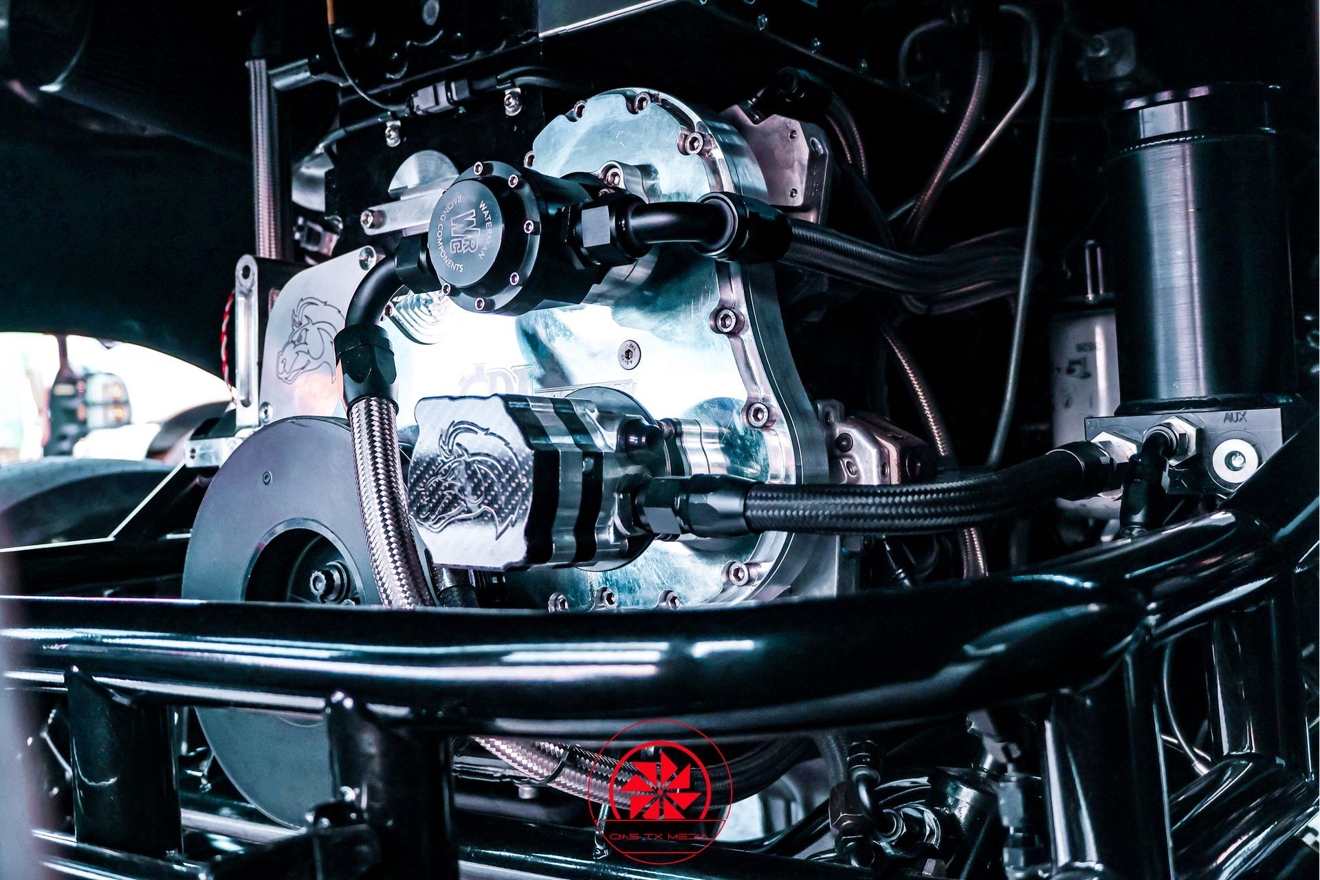 Polished engine in a car bay, surrounded by black tubing and wiring under bright lights