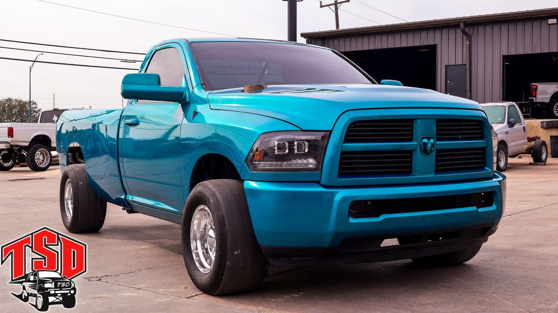 Bright turquoise lifted pickup truck parked outdoors at a dealership lot