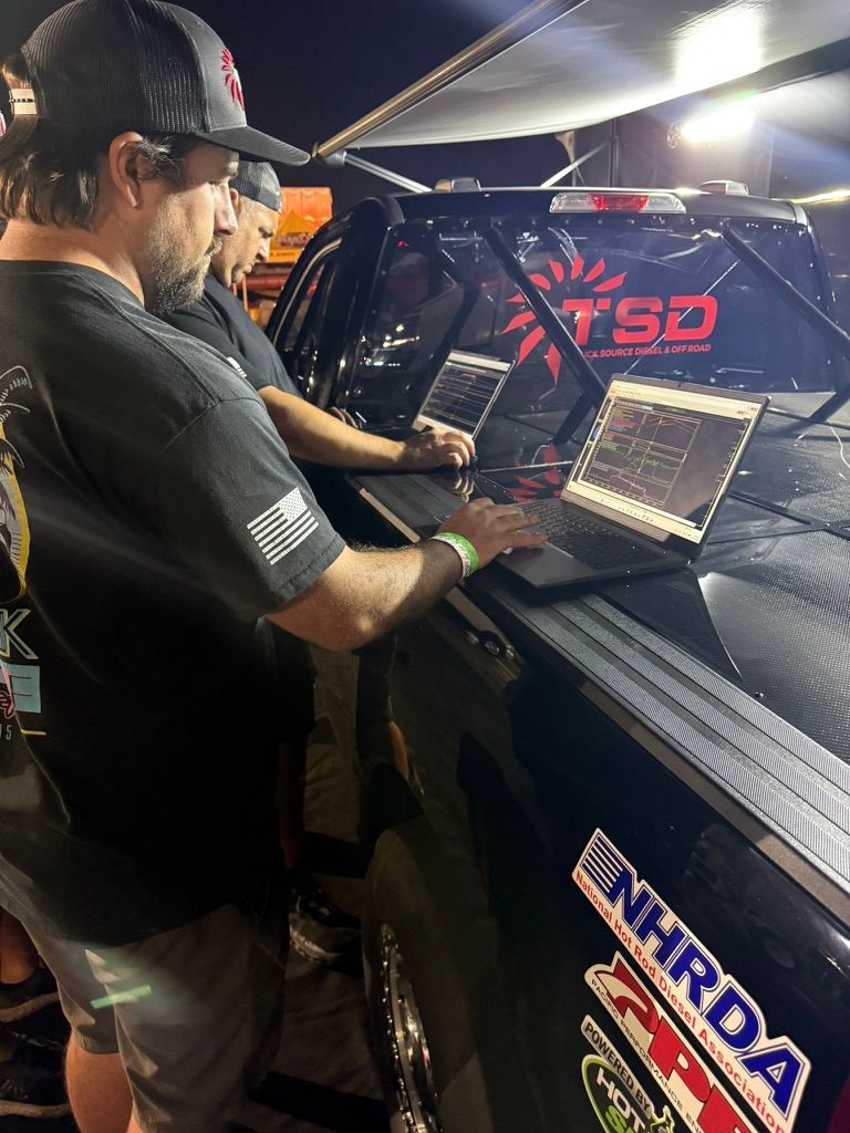 Technician working on a laptop beside a race car under bright garage lights