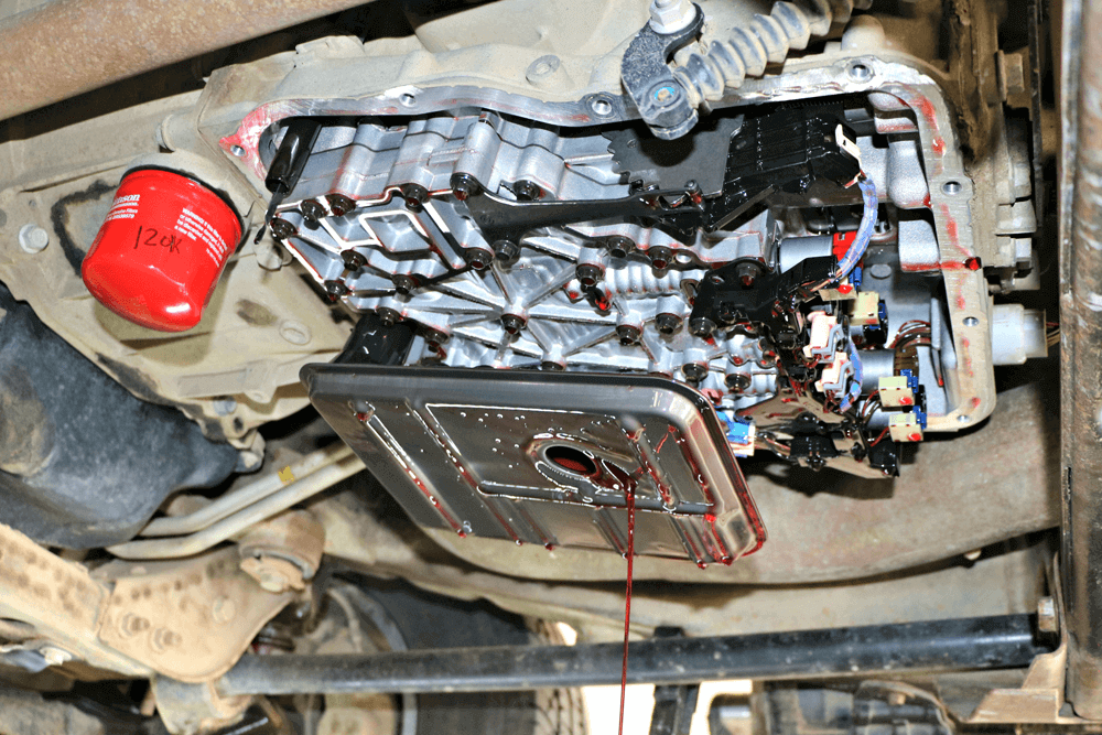 Undercarriage view of a vehicle with a damaged exposed transmission and a red oil filter.