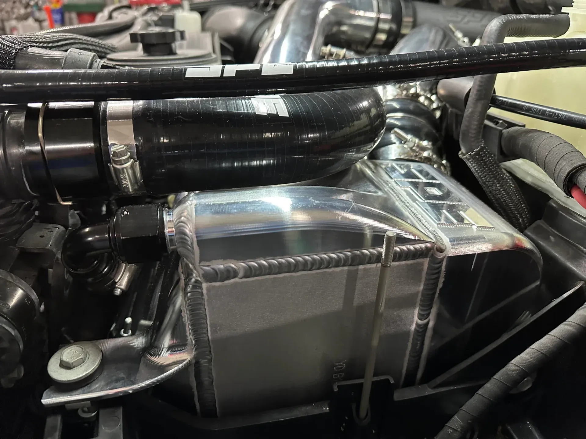 Close-up of a car engine component with black hoses and a silver metal box mounted in the engine bay