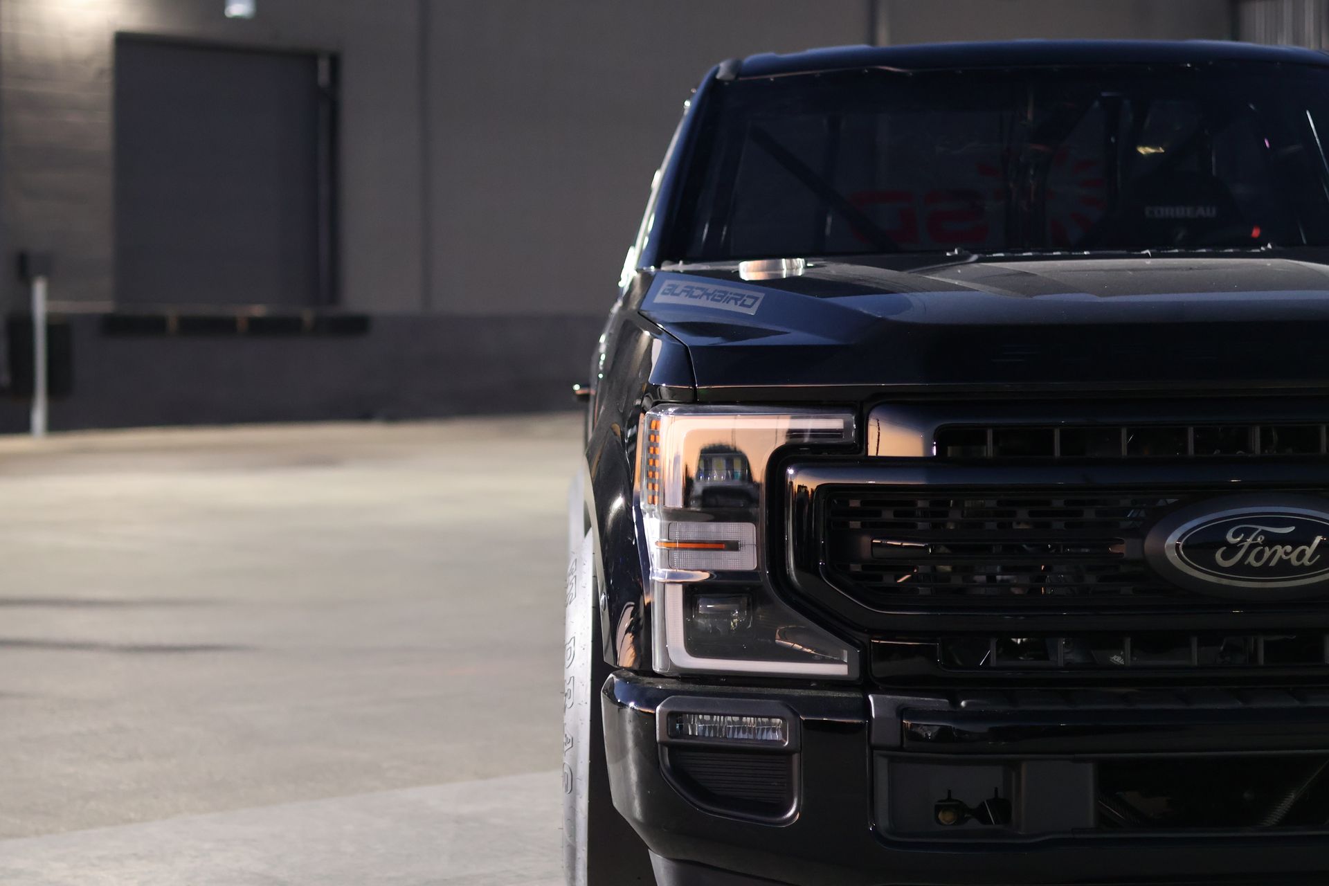 Black Ford pickup parked in a dim garage, front view on the right side of the frame