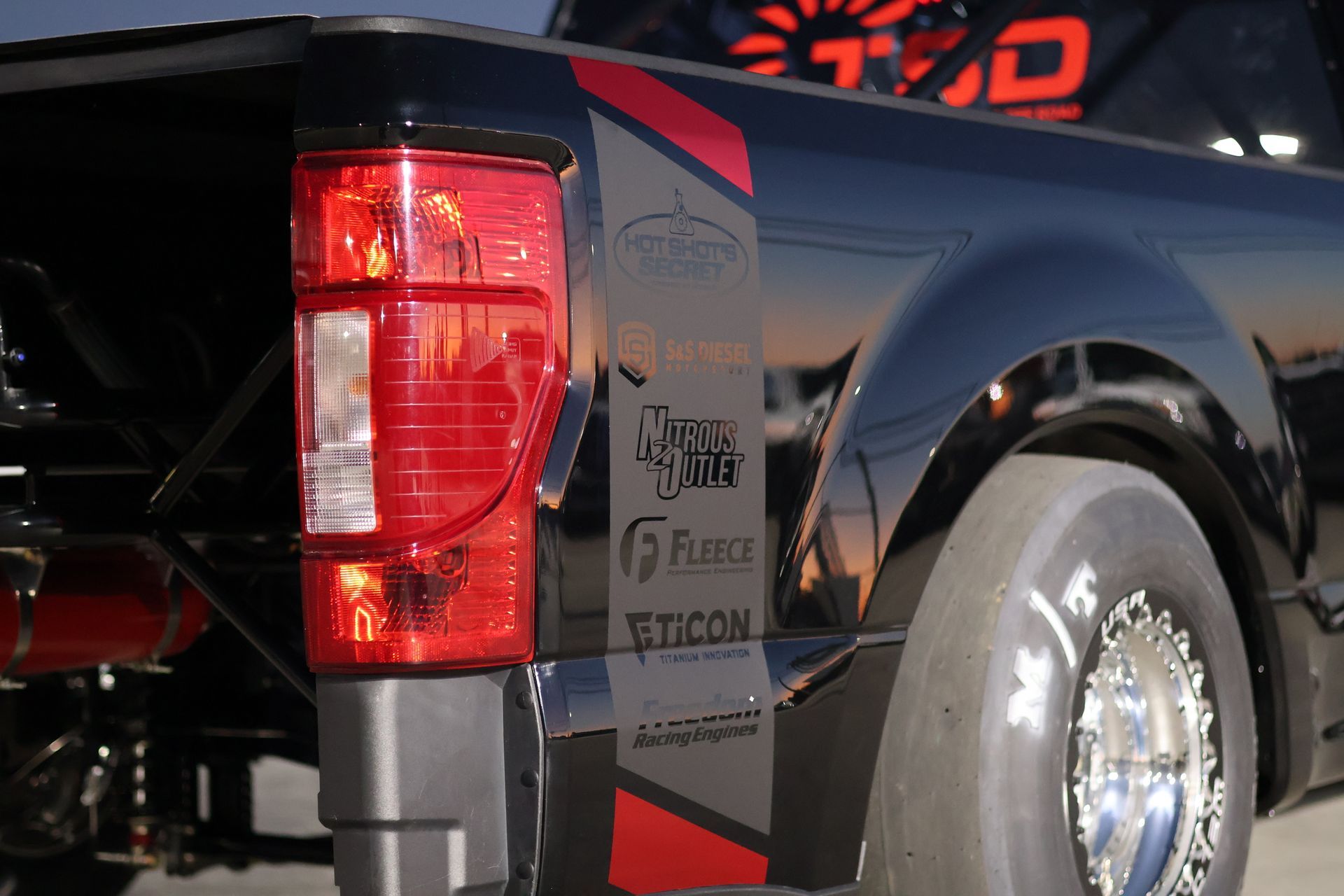 Close-up of a black pickup truck’s rear side with red taillight and chrome wheel in sunlight