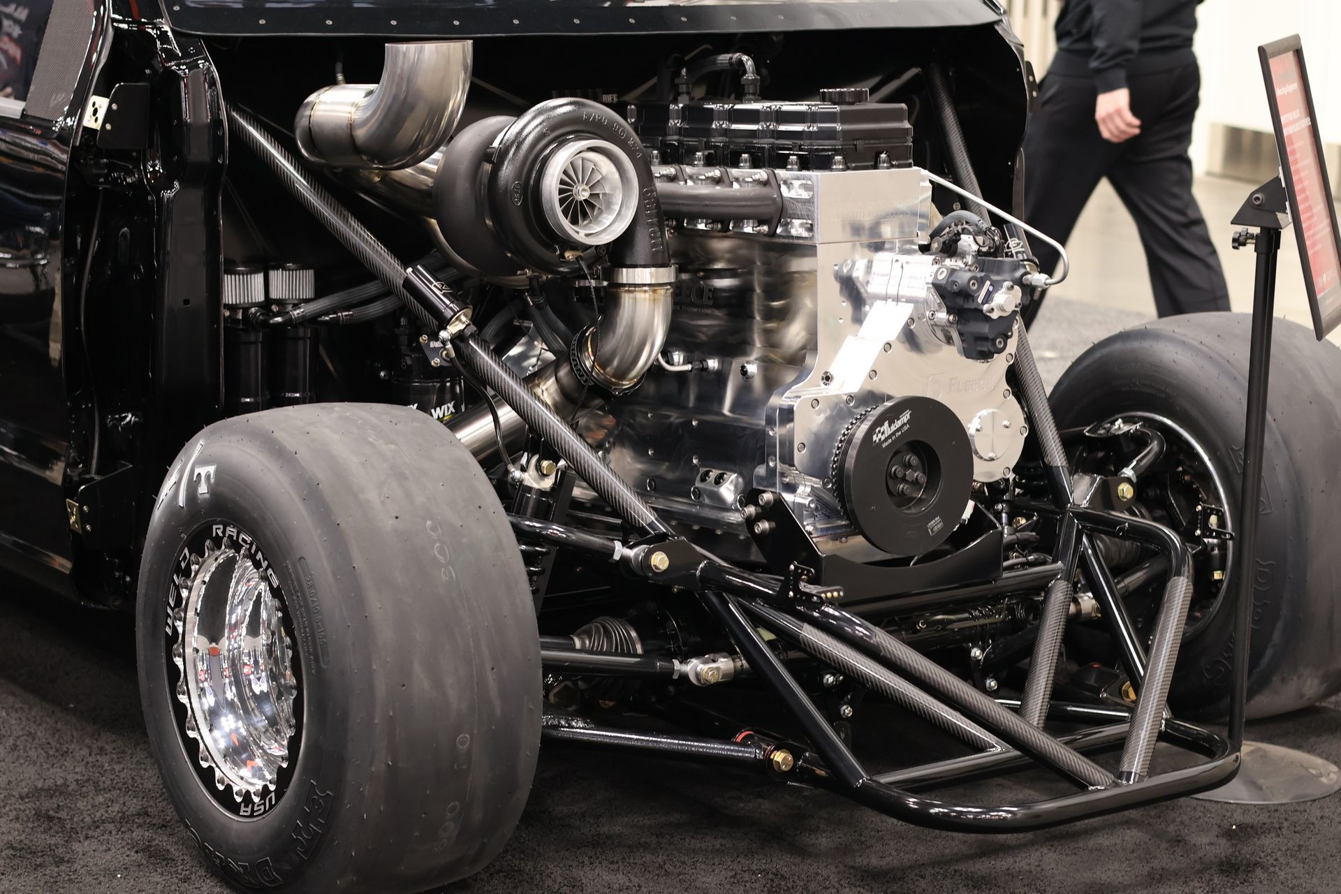 Close-up of a stripped race car with exposed engine and large rear tires in a garage.