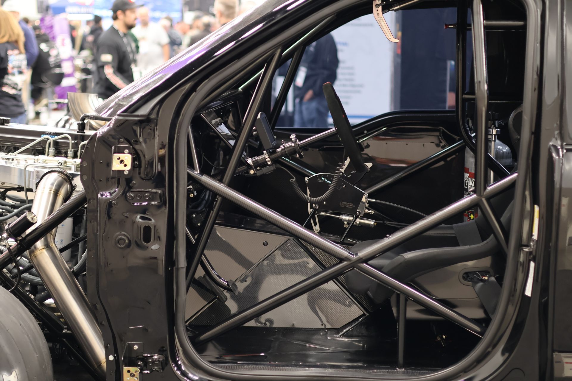 Race car interior with black roll cage and exposed frame at an auto show