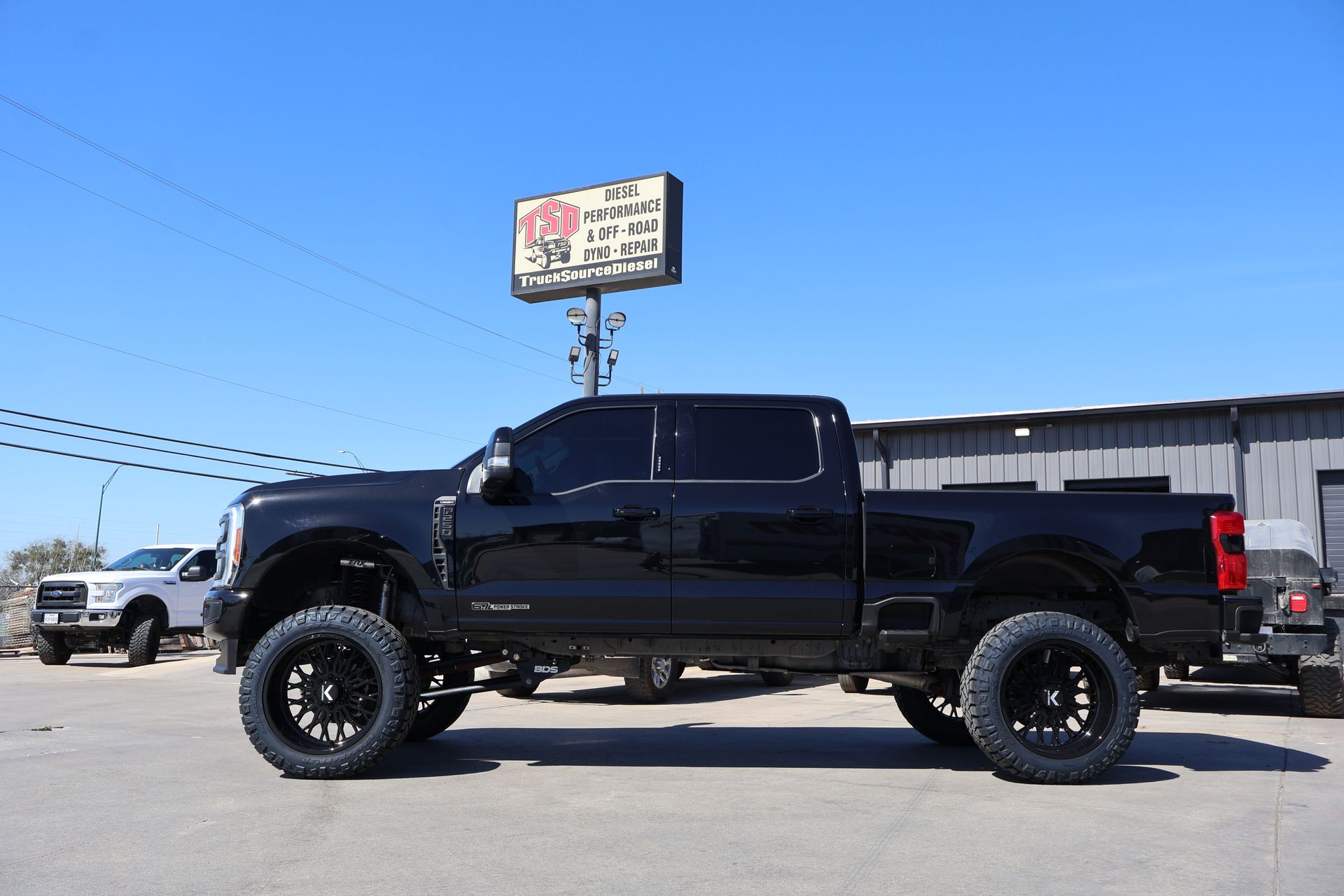 Black lifted pickup truck parked in a lot under a clear blue sky.