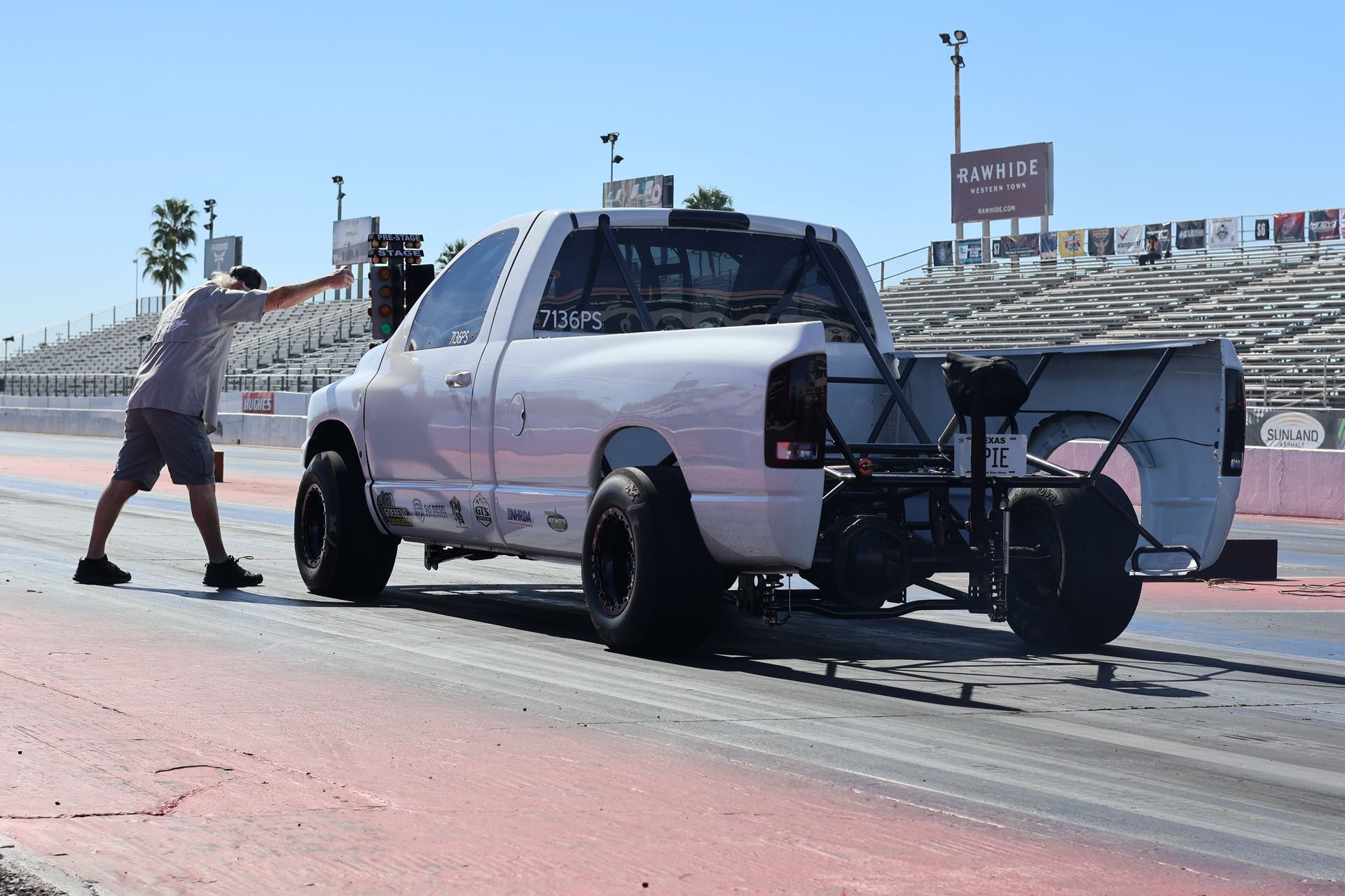 Person pushing a white pickup truck with a wheelie bar on a drag strip.