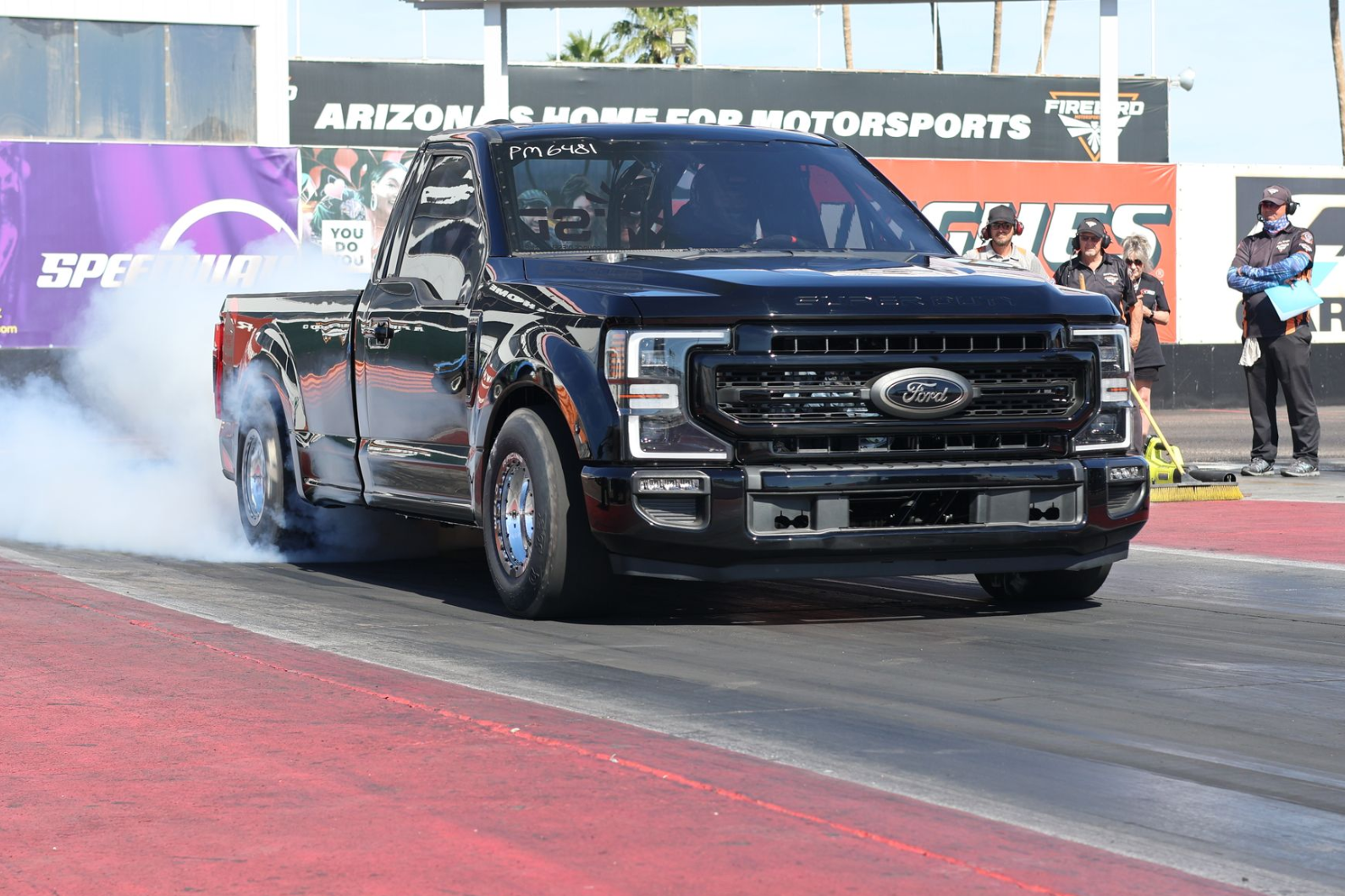 Black pickup truck doing a burnout on a drag strip with smoke billowing from the rear tires