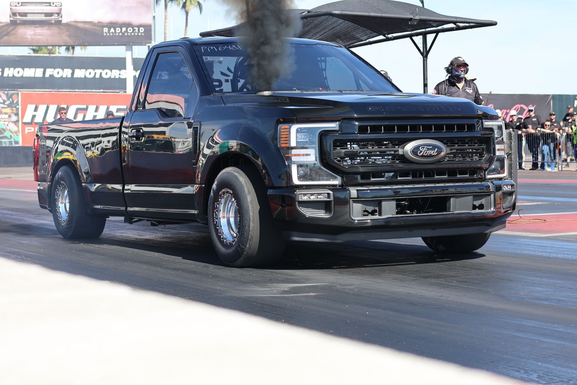 Black Ford pickup launching at a drag strip, front wheels lifted on the track.