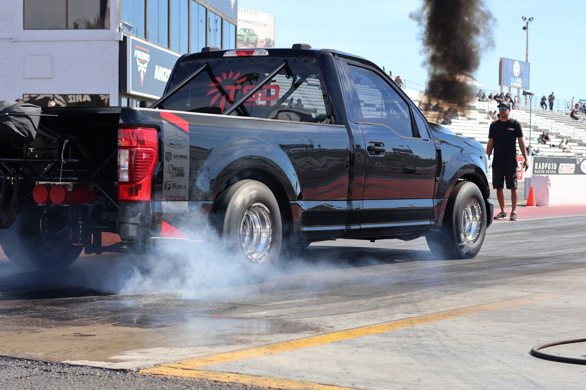 Black pickup truck doing a burnout on a race track, with smoke billowing from the rear tires.