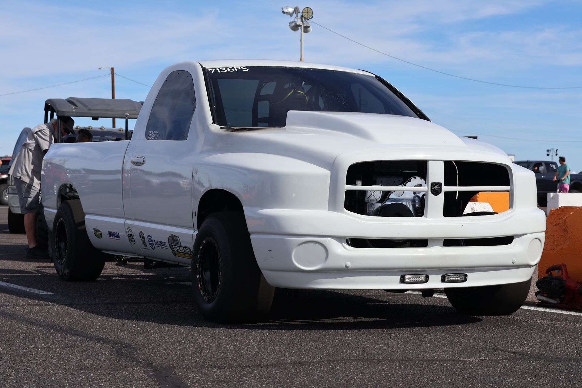 White pickup truck with a stripped front grille parked on a road under a blue sky