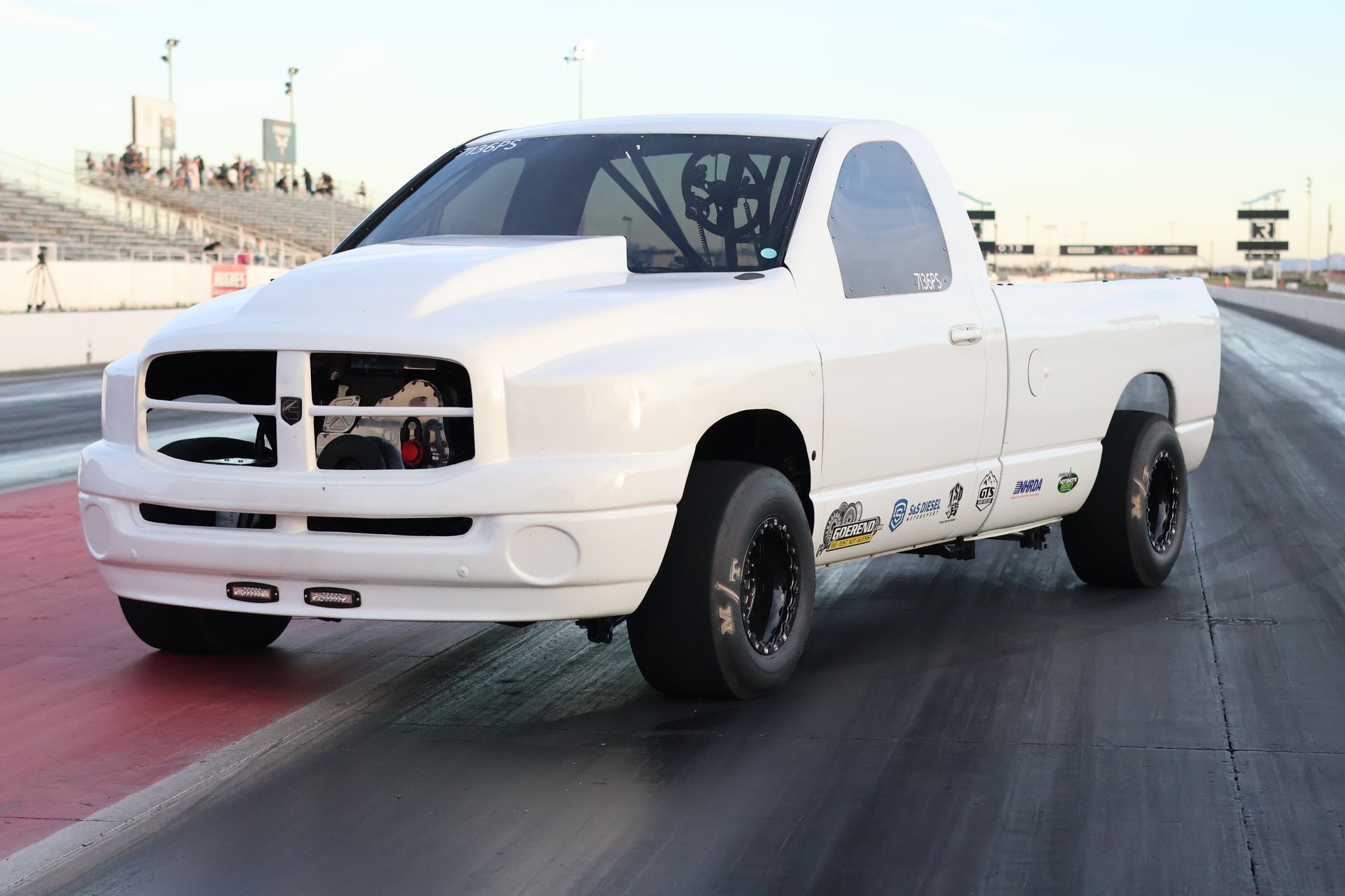 White drag racing pickup truck on a track, front end removed, with black wheels and a racing strip visible