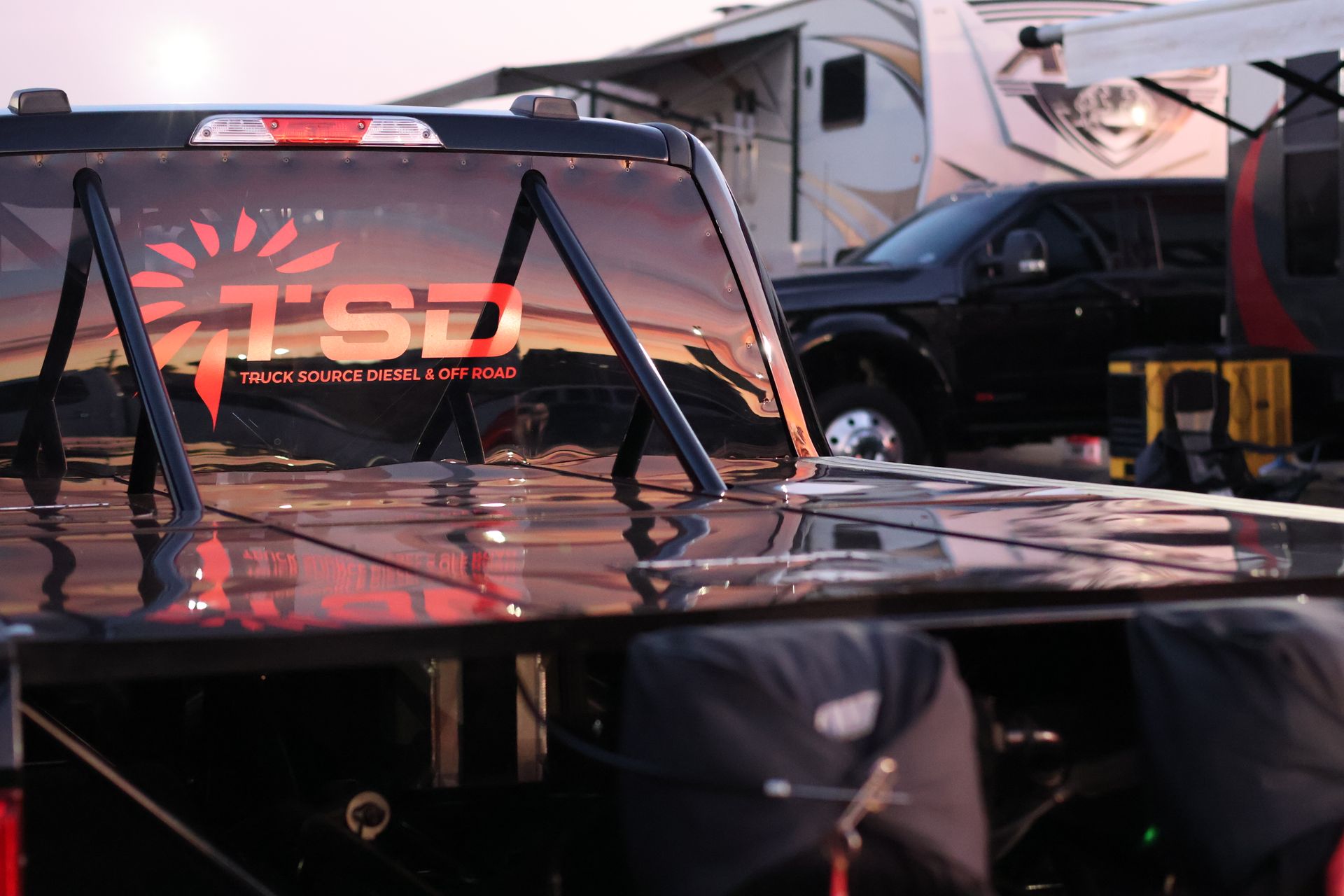 Black off-road race truck with roll cage and TSI logo parked on a dirt track at sunset