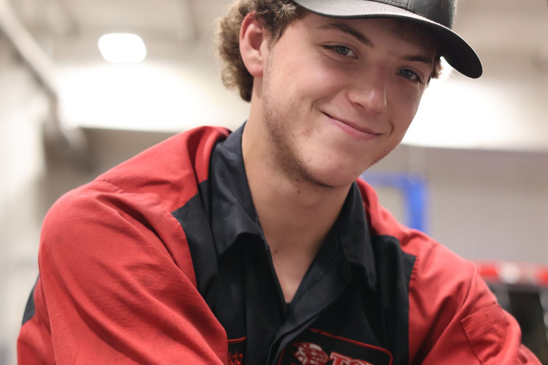 Maddox Drager in a red and black uniform shirt and black cap, leaning forward indoors.