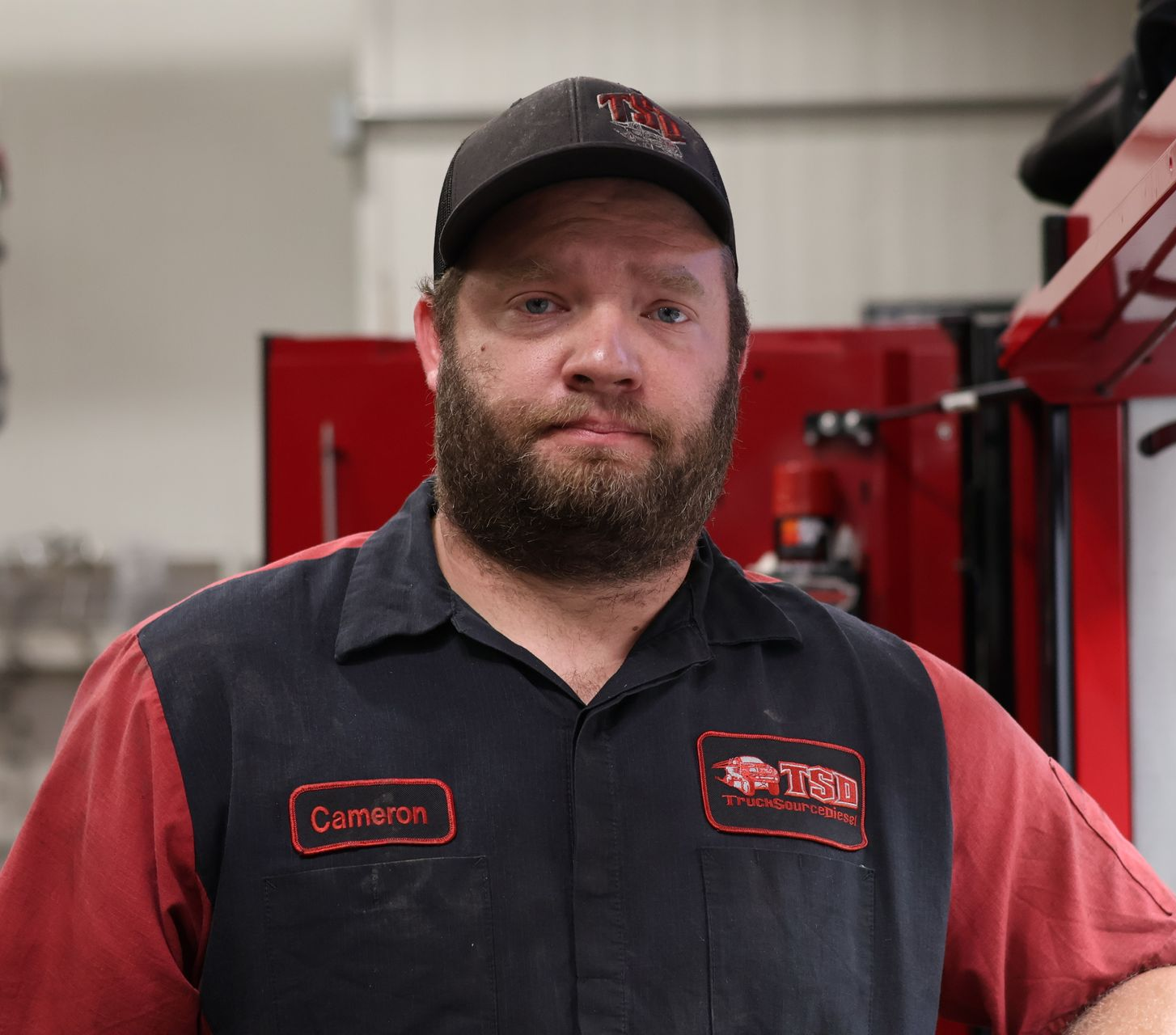 Cameron Jones in the shop, wearing a black-and-red uniform and cap, with red equipment behind him