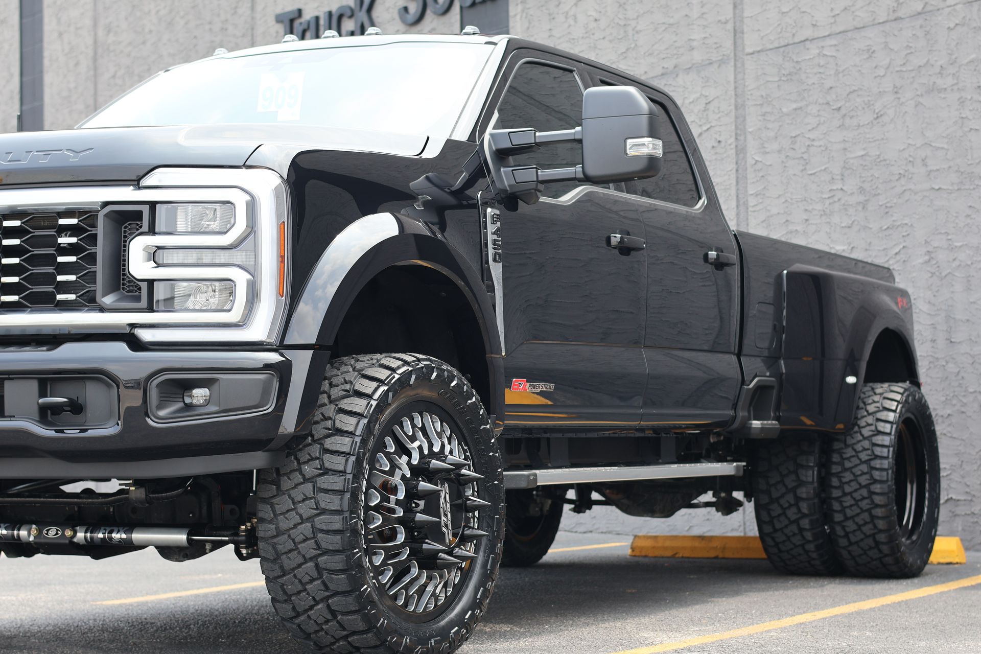 Black lifted pickup truck parked on a street, front-left view with oversized off-road tires.