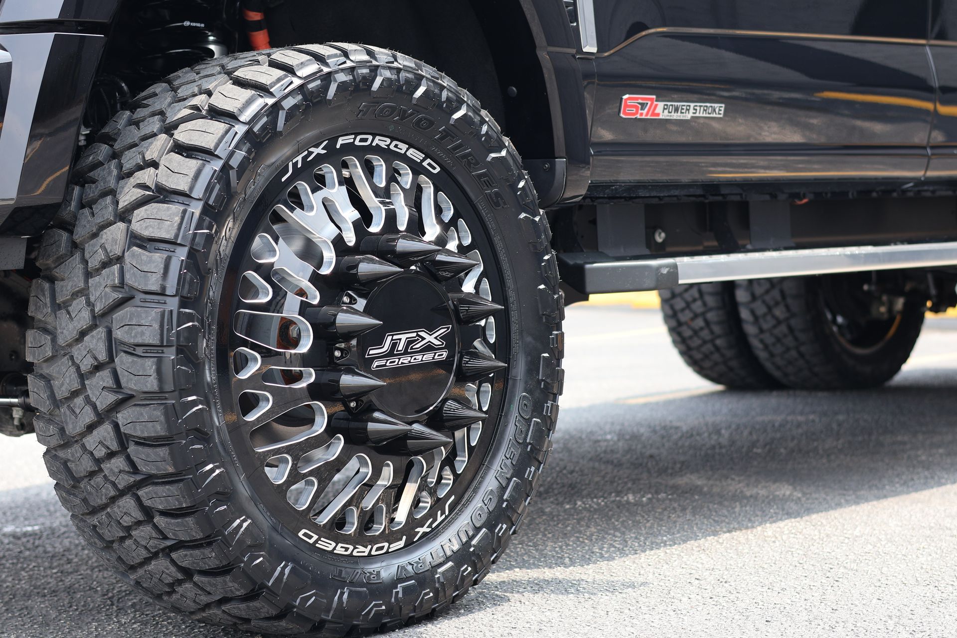 Close-up of a black lifted truck’s front wheel with large off-road tire and chrome rim.