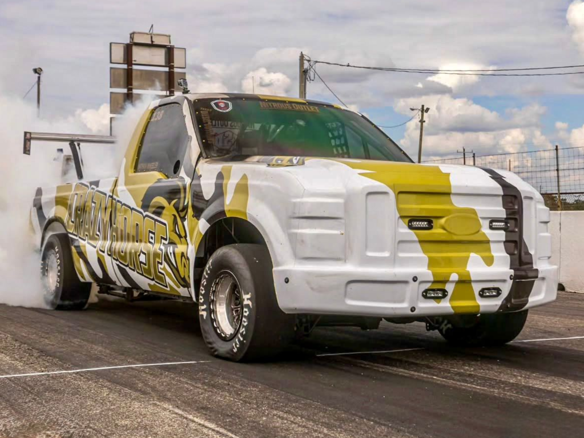 White and yellow diesel-powered drag truck named CrazyHorse doing a burnout on a racetrack