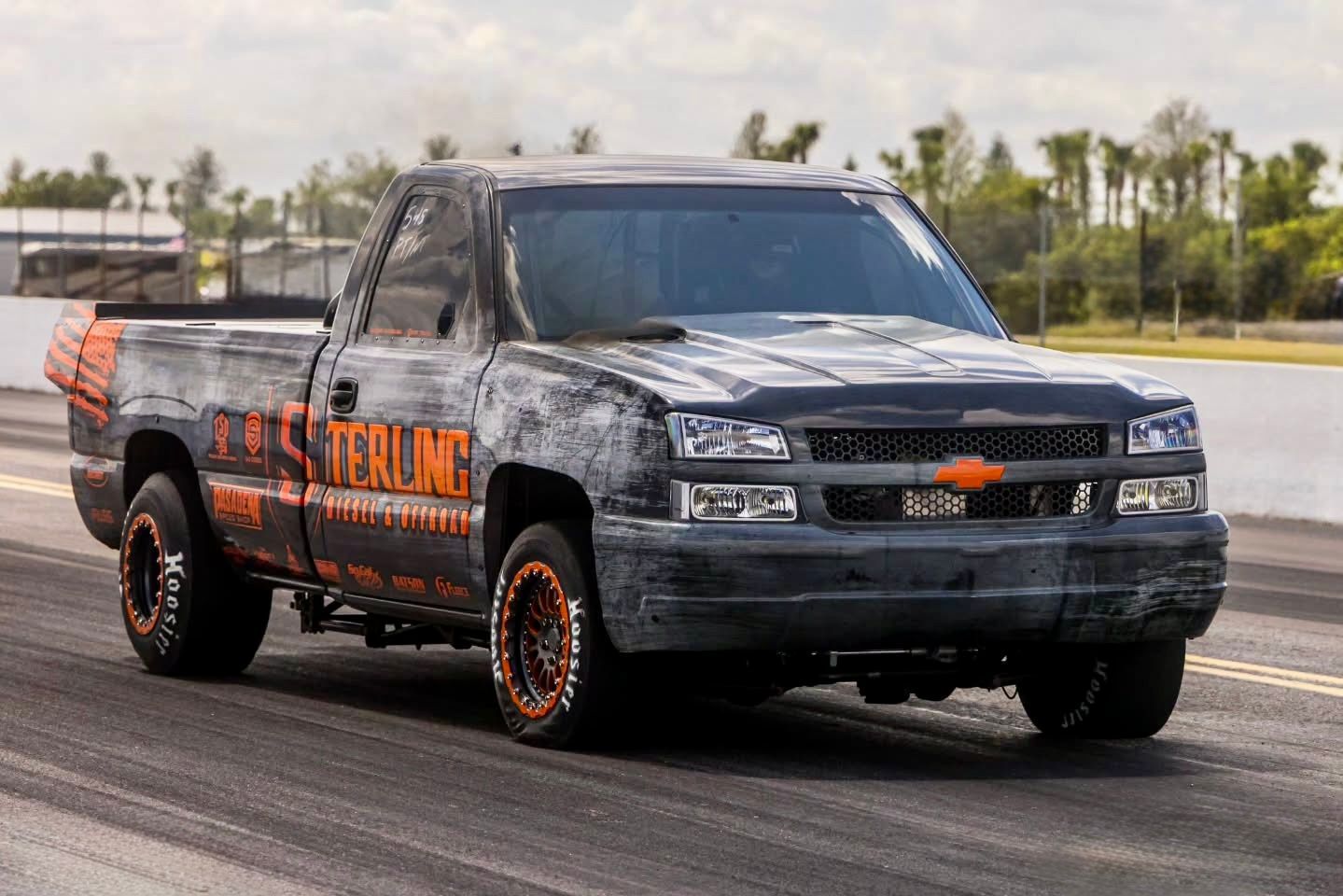 Black Chevrolet pickup truck with orange graphics driving on a track or road.