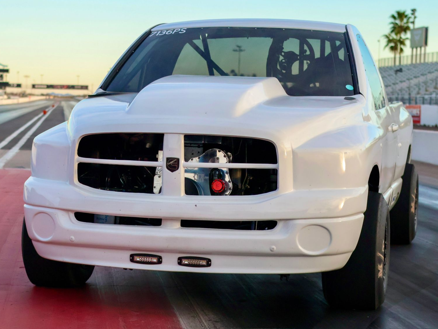 White diesel-powered race truck named Opie driving on a racetrack at sunset