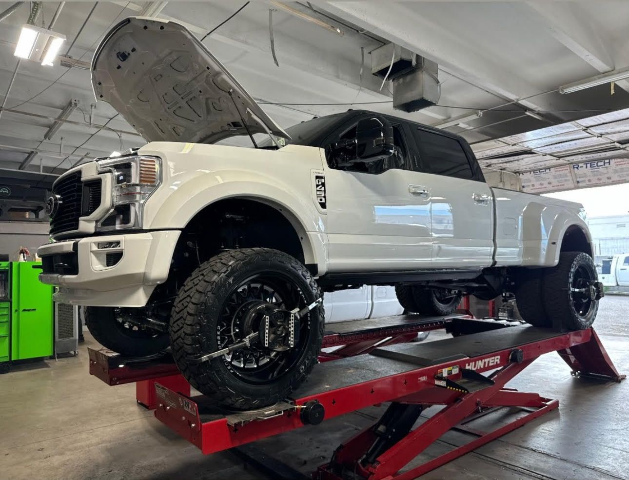 White pickup truck on a red lift in an auto shop with its hood open