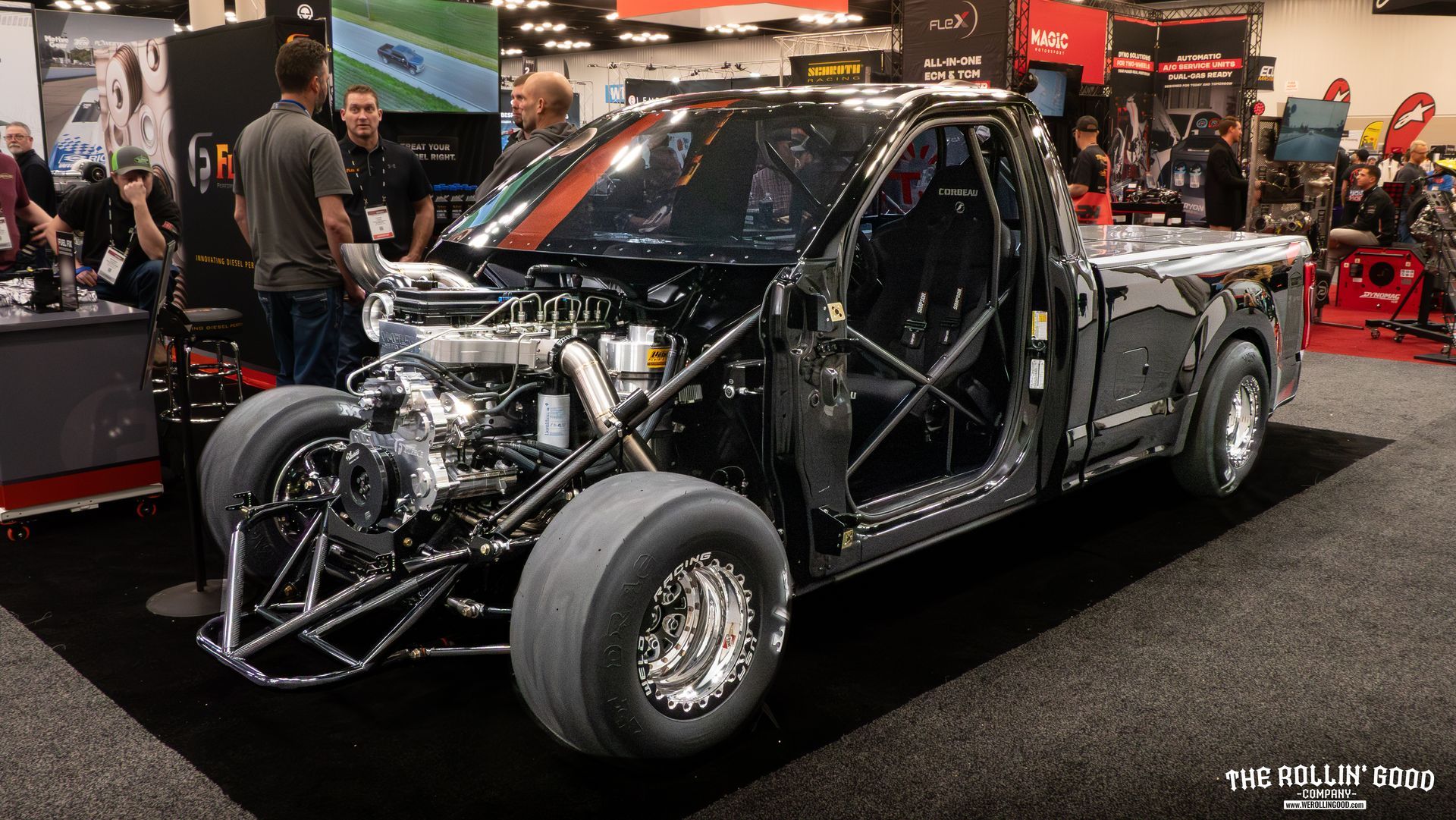 Black hot rod drag car at an indoor auto show, with exposed engine and roll cage