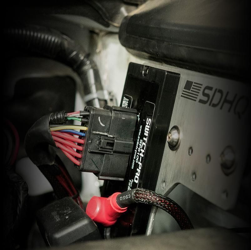 Close-up of a wiring harness and black connector mounted beside an SDH-branded metal panel.