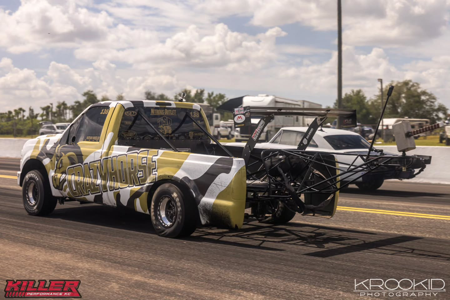 Two customized off-road race trucks parked on a drag strip under a cloudy sky