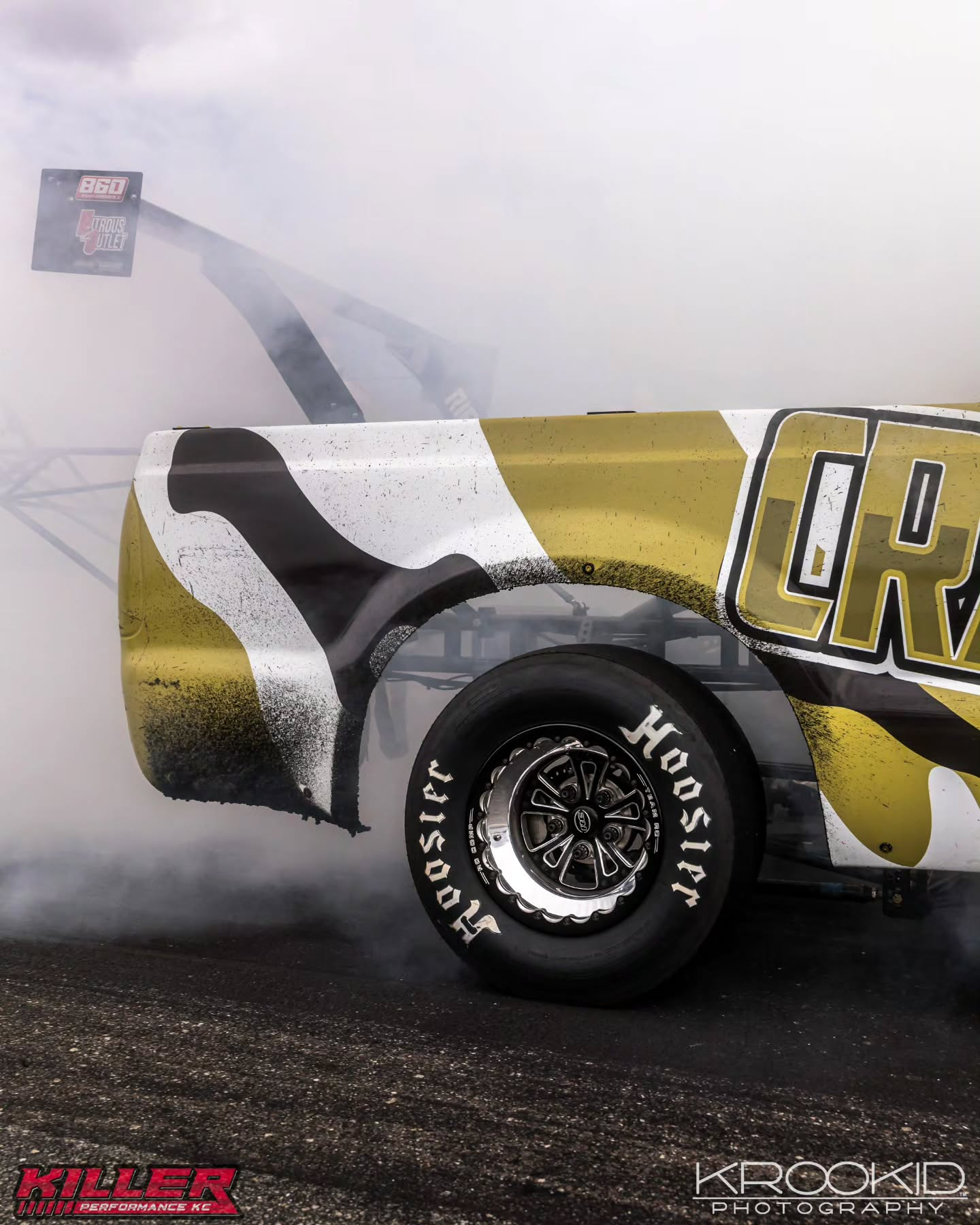 Yellow-and-black drag racing car tire spinning in smoky burnout on a track