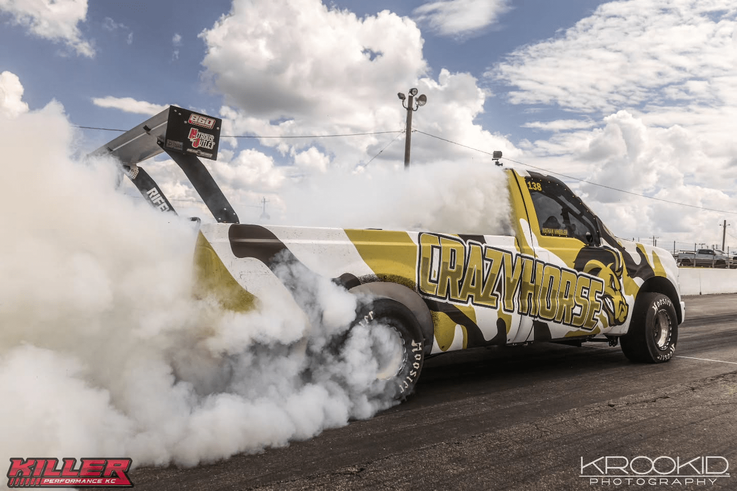 White and yellow drag racing pickup truck doing a burnout, thick smoke billowing on a racetrack