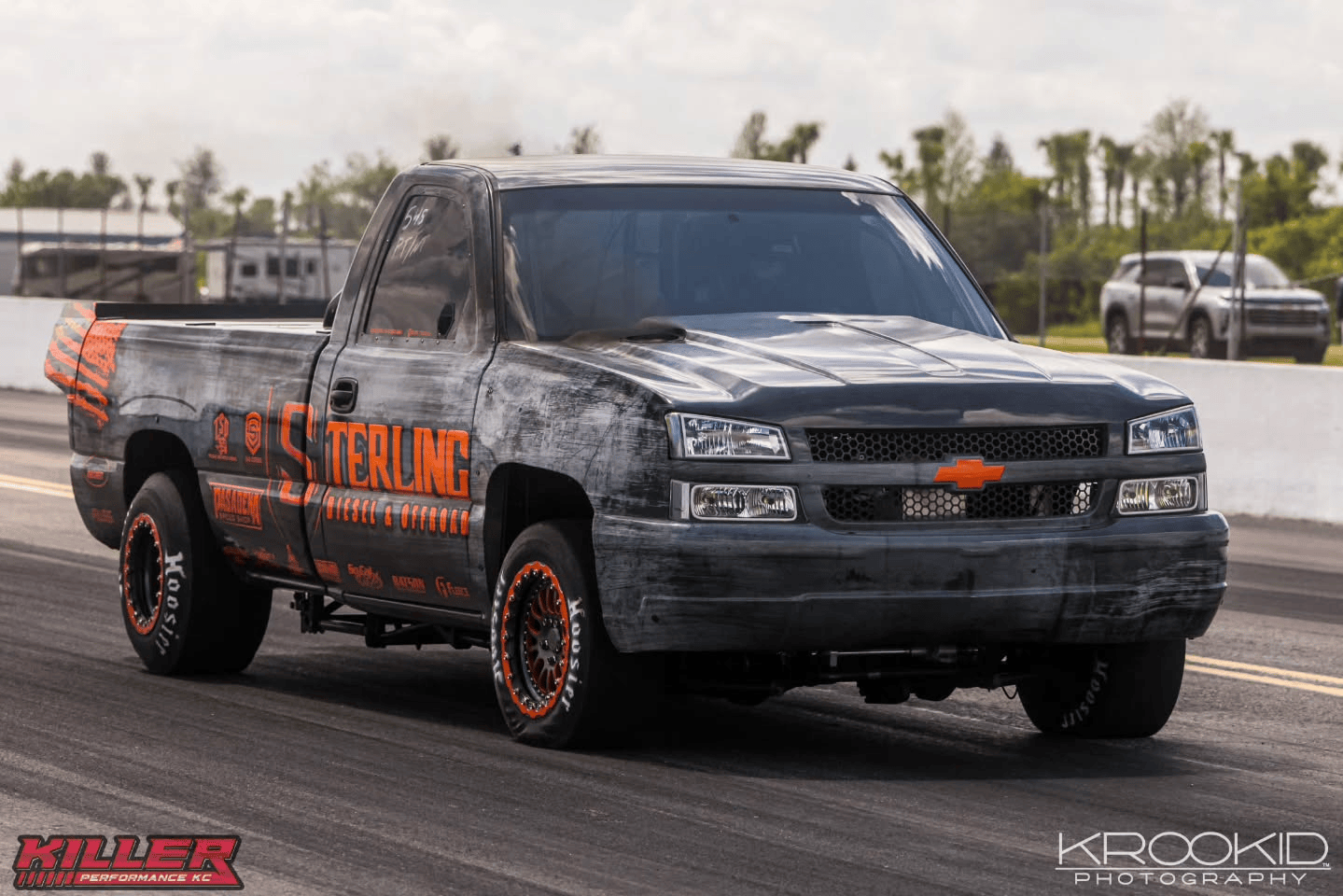 Black Chevrolet pickup truck with orange graphics racing on a drag strip
