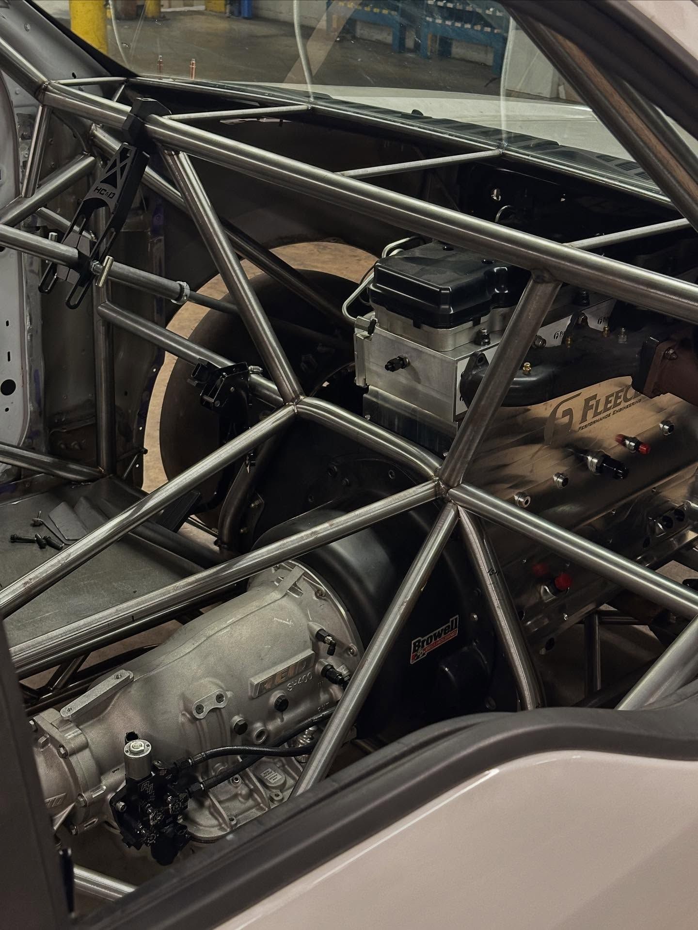 Race car interior with a exposed roll cage and mechanical drivetrain components inside the chassis