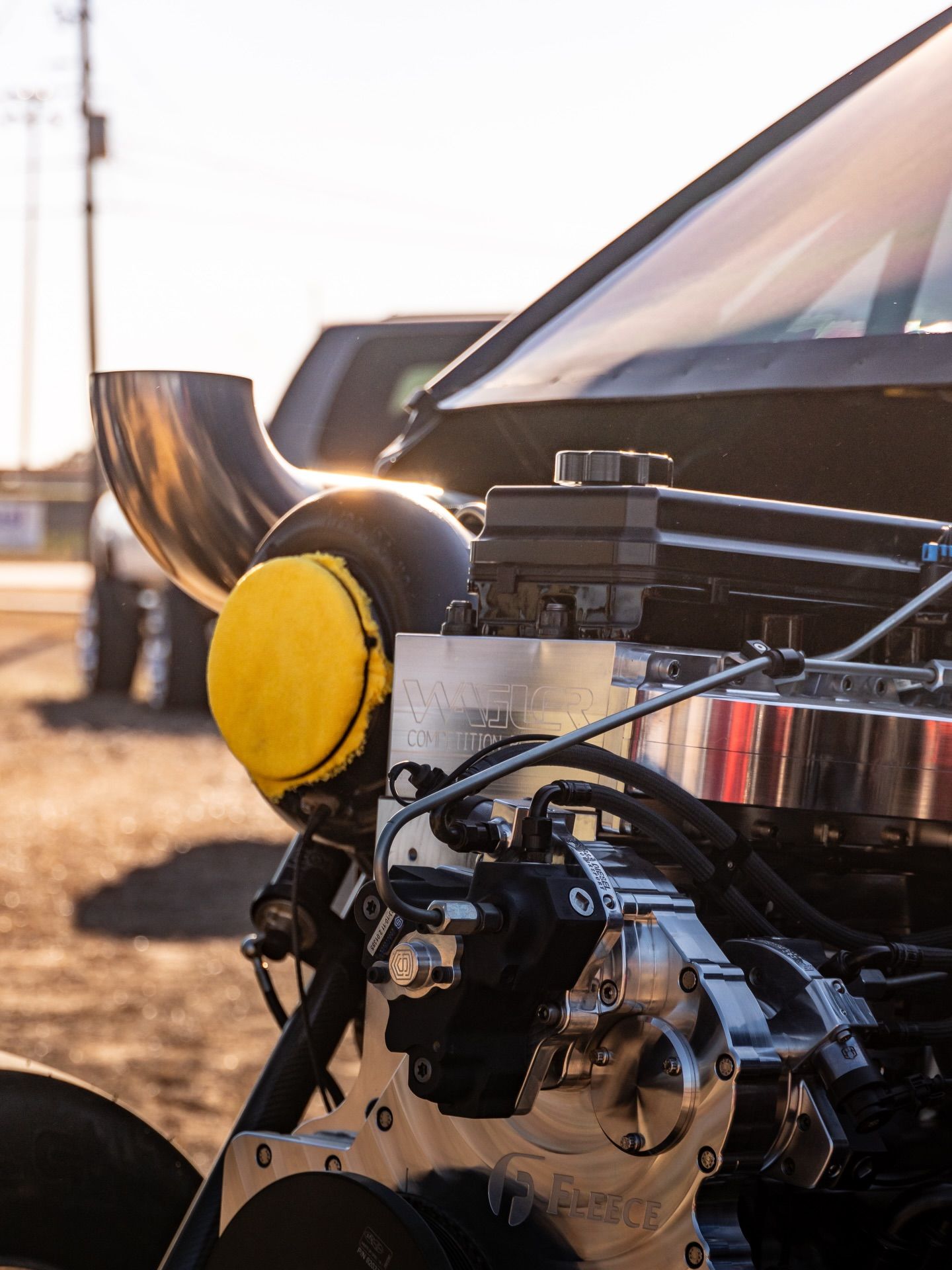 Close-up of a car engine with a yellow air intake and chrome components in sunlight