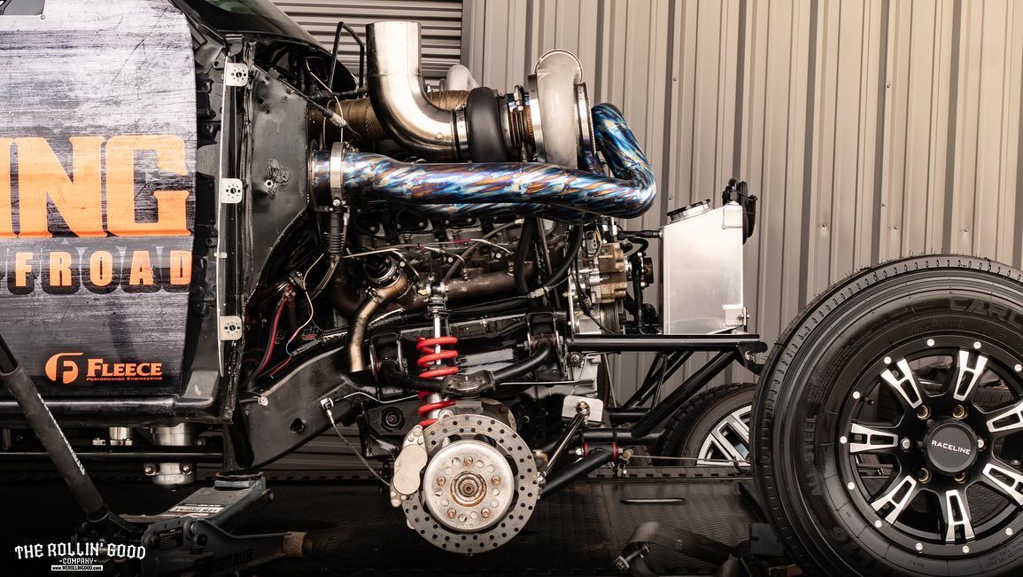 Black custom truck with exposed engine and chrome exhaust, side view at a car show