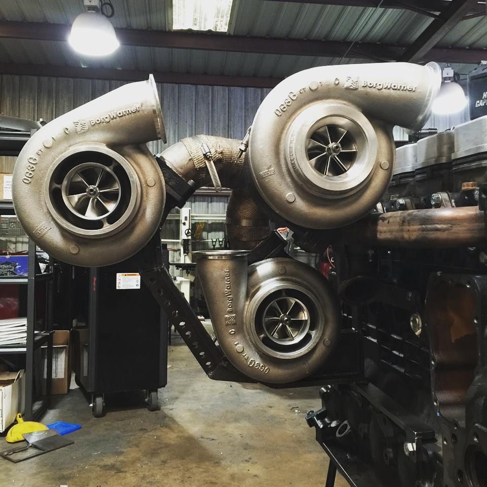 Twin large turbochargers mounted on an engine in a workshop, with exposed piping and industrial lighting.
