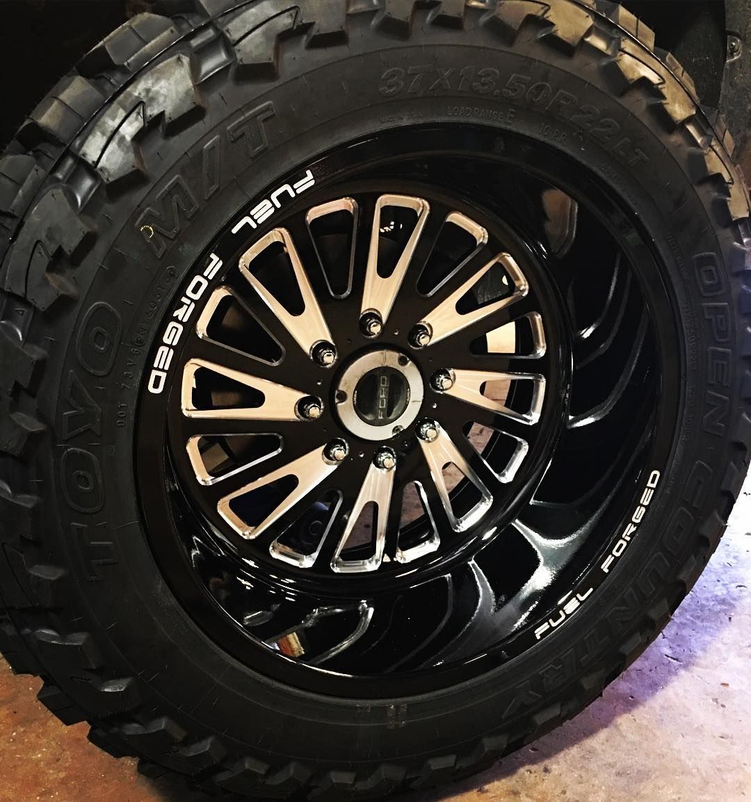 Close-up of a black off-road tire and alloy wheel on a vehicle, with rugged tread and white sidewall lettering