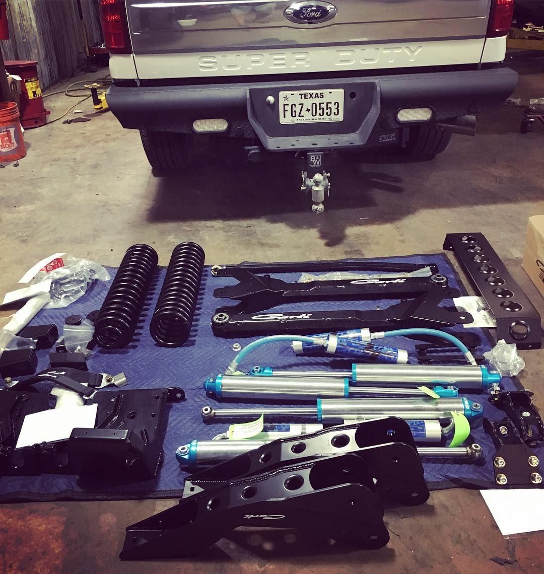 Car suspension parts and tools laid out on a garage floor beneath a silver pickup truck.