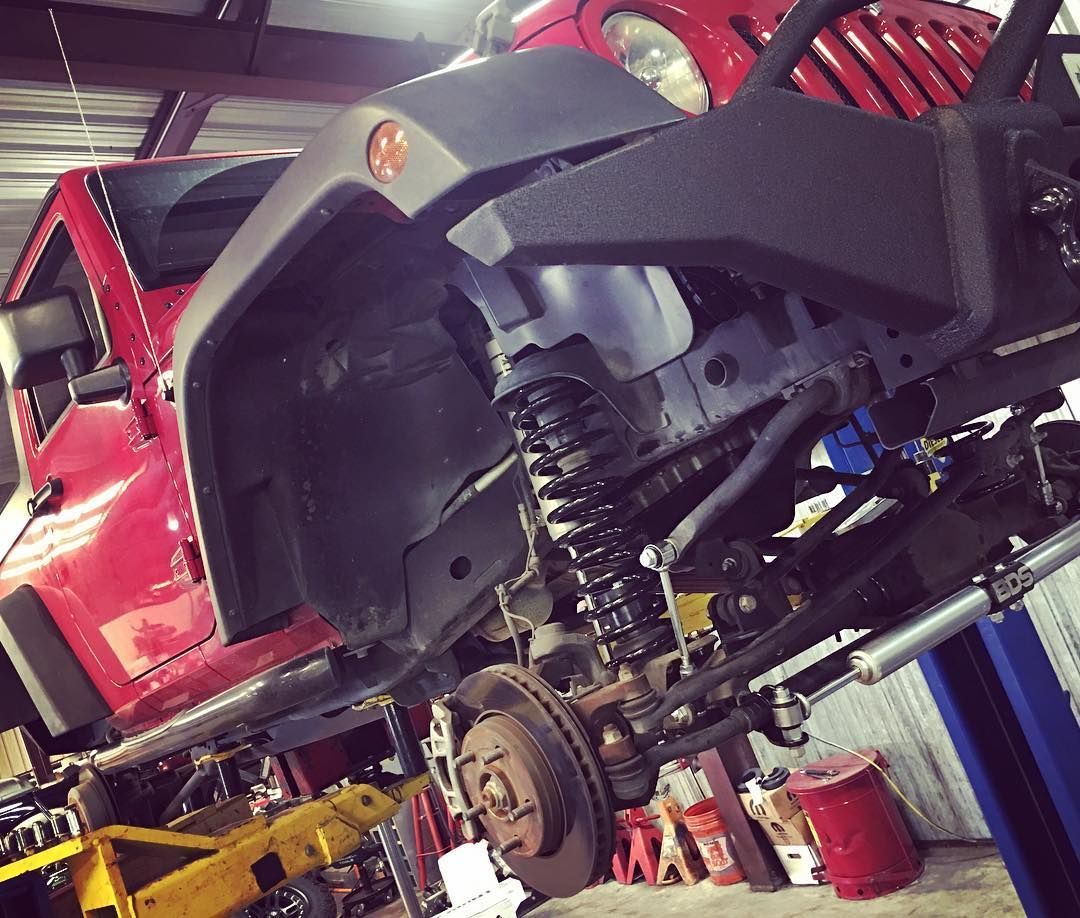 Lifted red off-road vehicle in a garage, showing exposed suspension and wheel well.